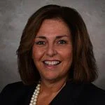 Smiling woman with brown hair wearing a dark blazer and pearl necklace