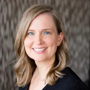 Smiling person with shoulder-length hair and a blurred background.
