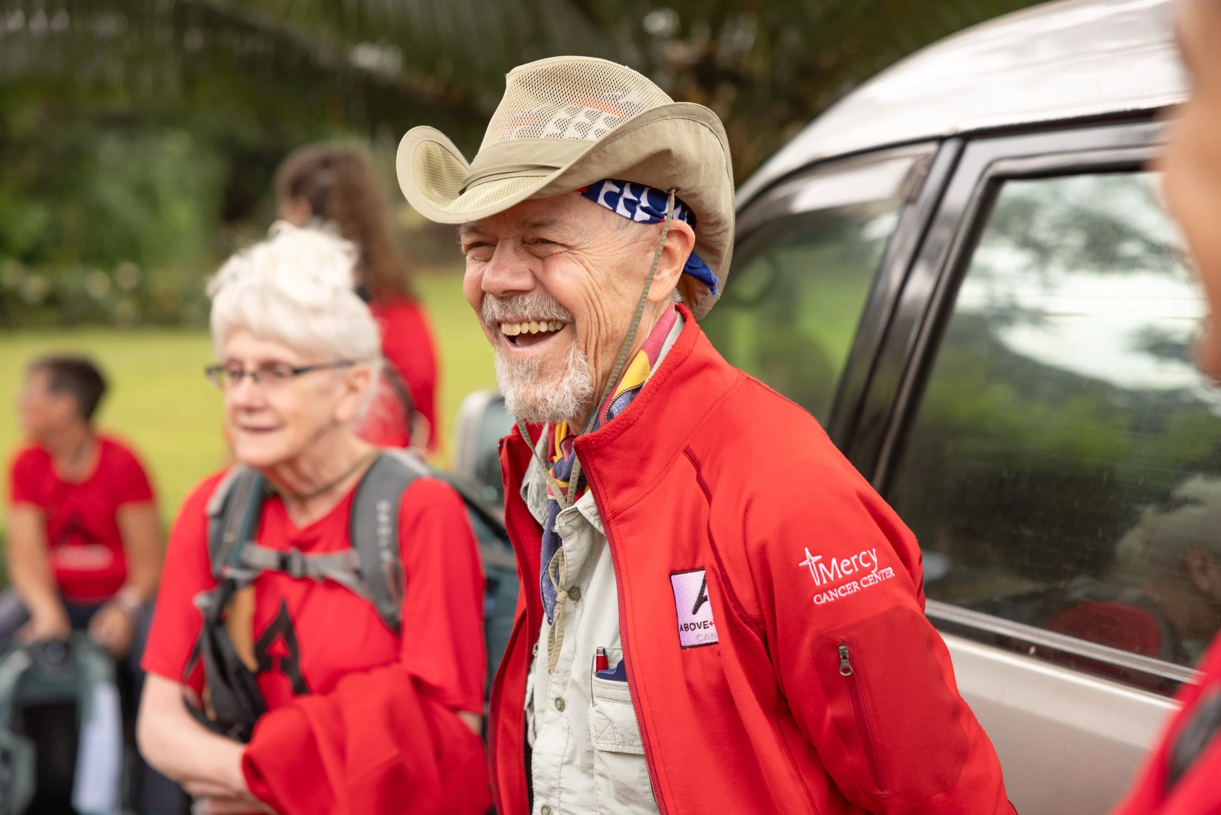 Group of people in red jackets outdoors, with one man wearing a cowboy hat smiling.