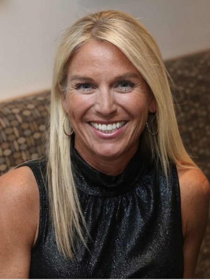 Smiling woman with blonde hair wearing a black sleeveless top and hoop earrings.
