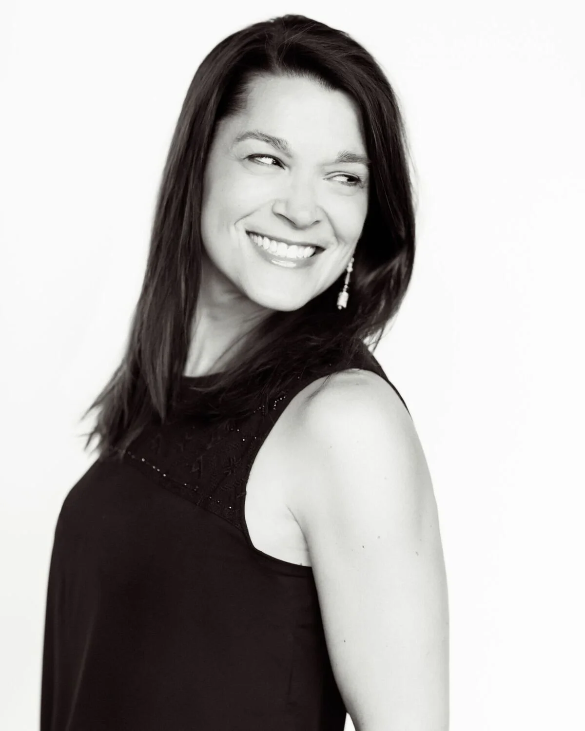 Smiling woman with long dark hair wearing a sleeveless top, looking to the side in a black and white photo.