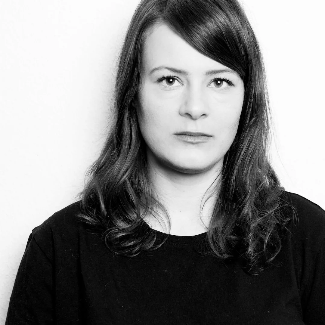 Black and white portrait of a woman with shoulder-length wavy hair, wearing a dark top, against a plain light background.