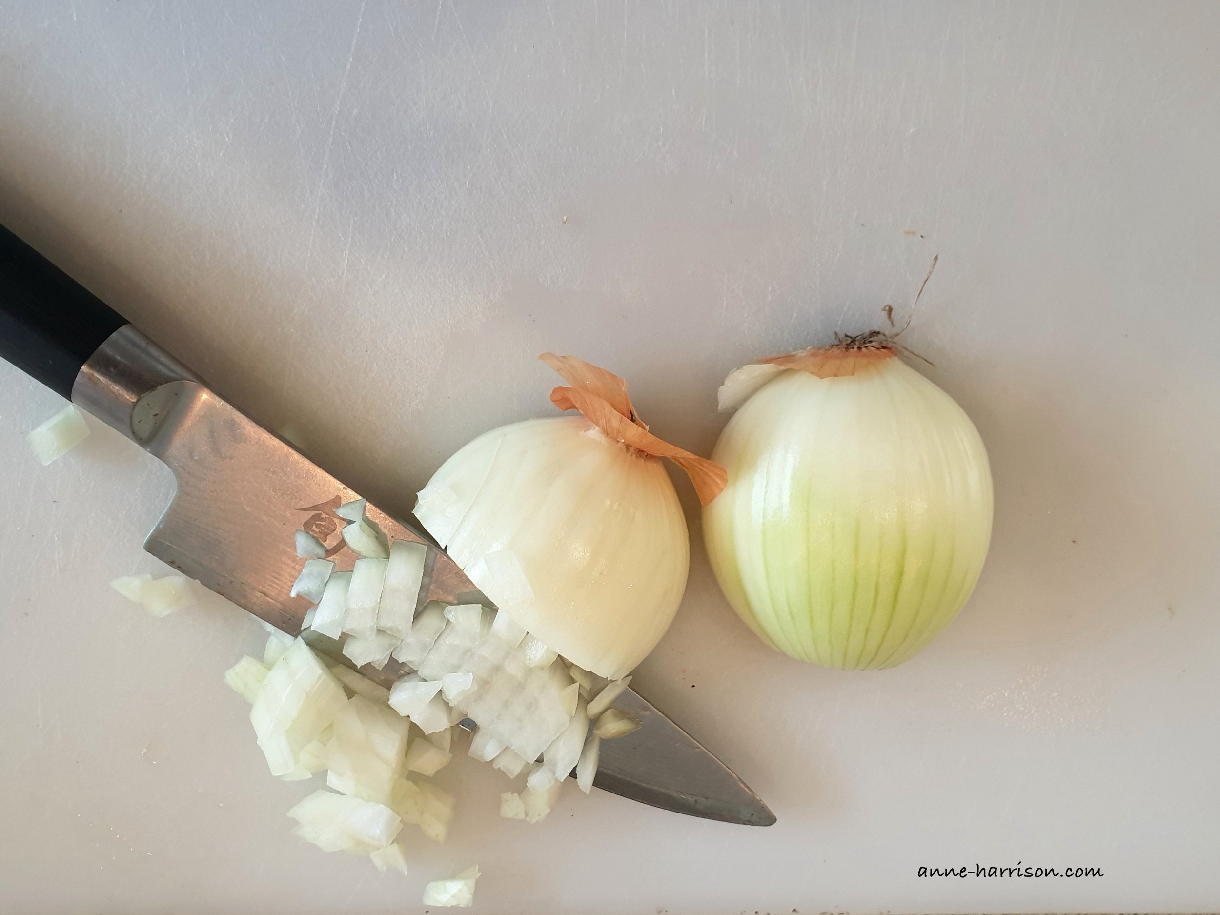 two halves of a white onion. One is partially diced, and a Japanese knife is next to them.
