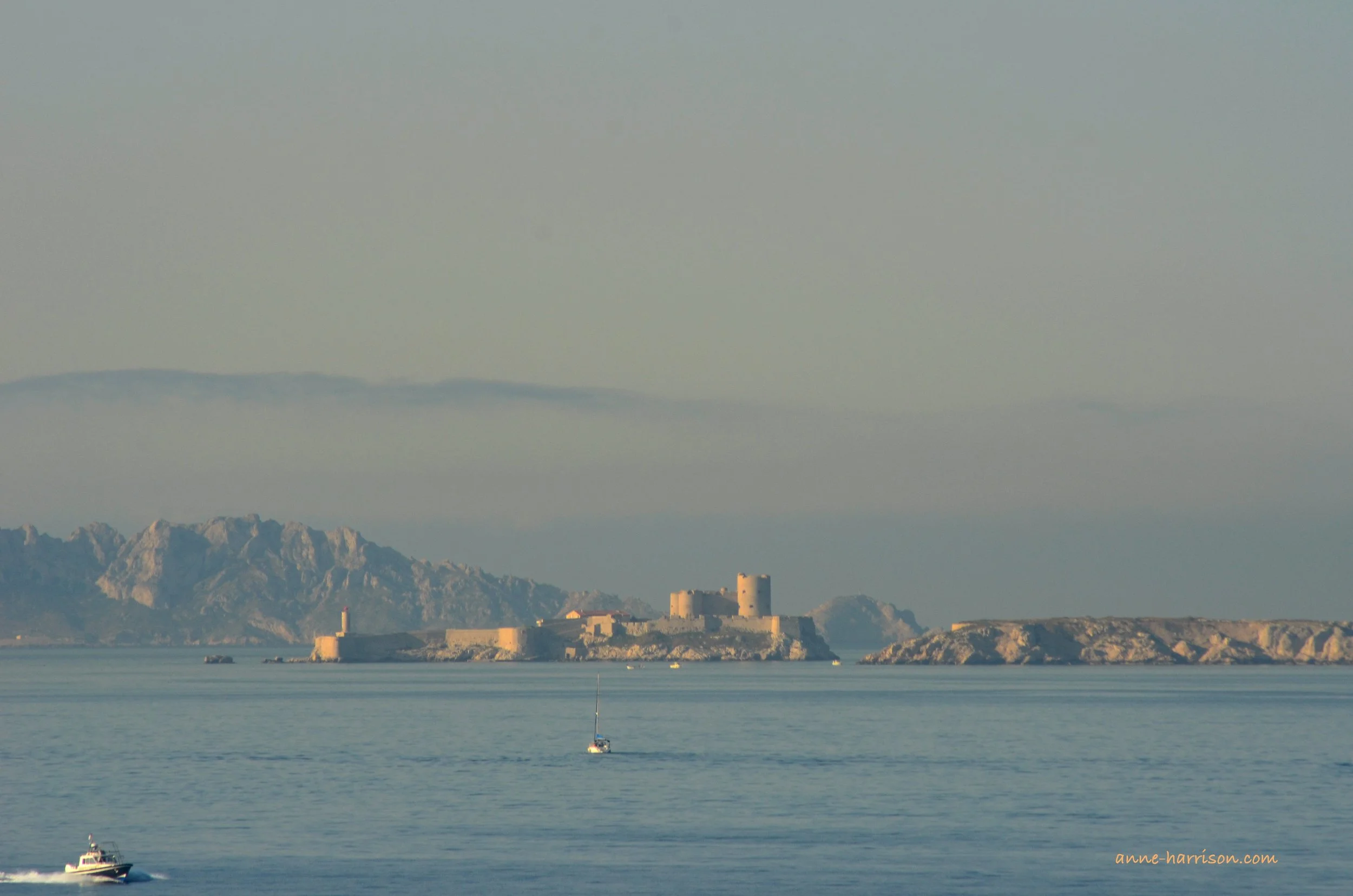 The Chateau D'if, in the waters off Marseille. Small rocky islands surround it, and some boats are in the foreground, showing its size.