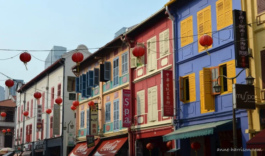 Traditional buildings in Singapore, with colourful facades and window shutters. Red lanterns hang are strung the street.