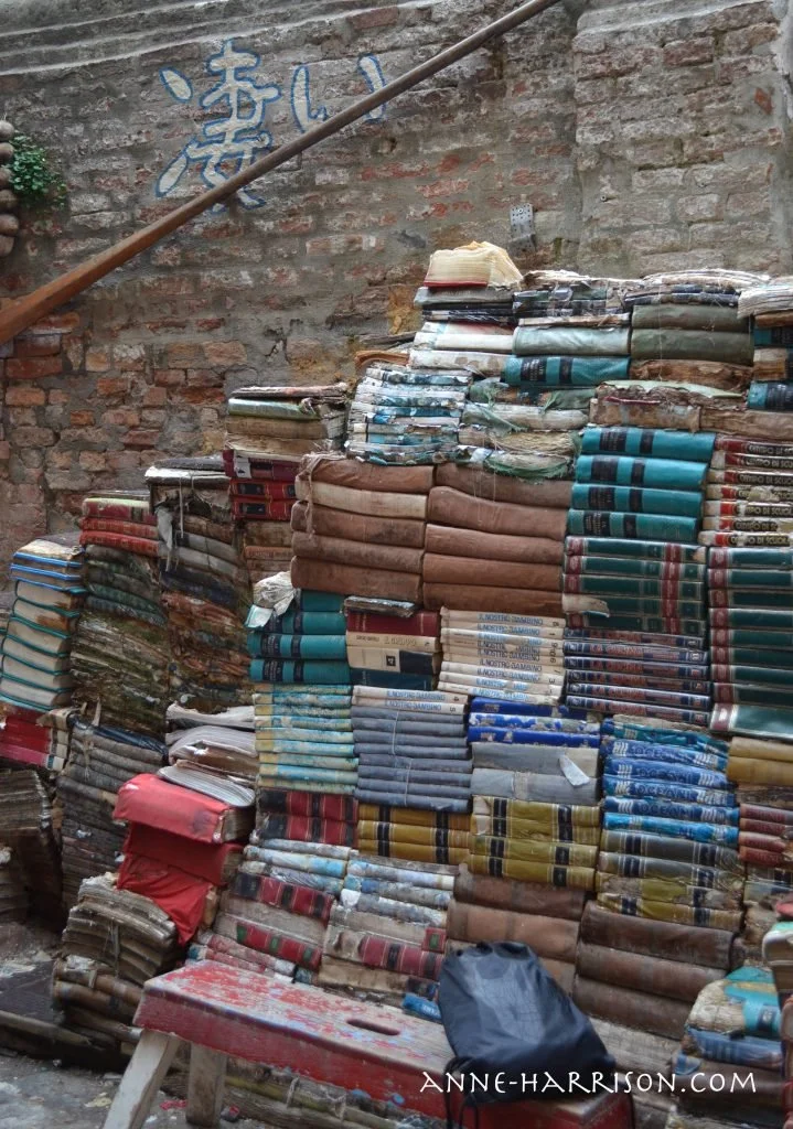 Old books stacked to make a staircase beside a brick wall