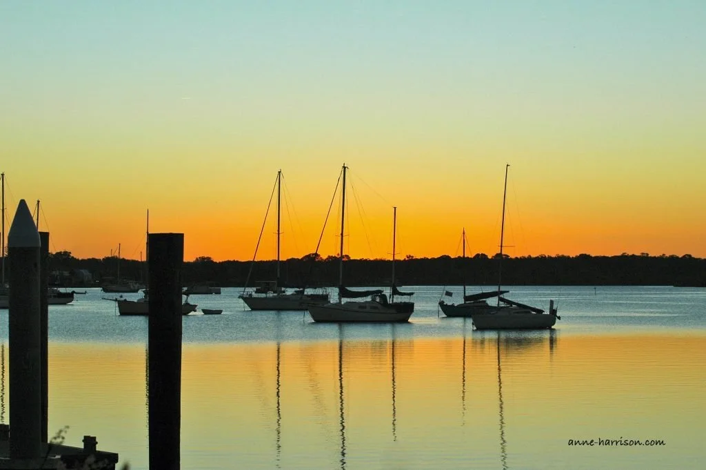 Boats on a river at sunset, with the colours of the sky reflected in the water