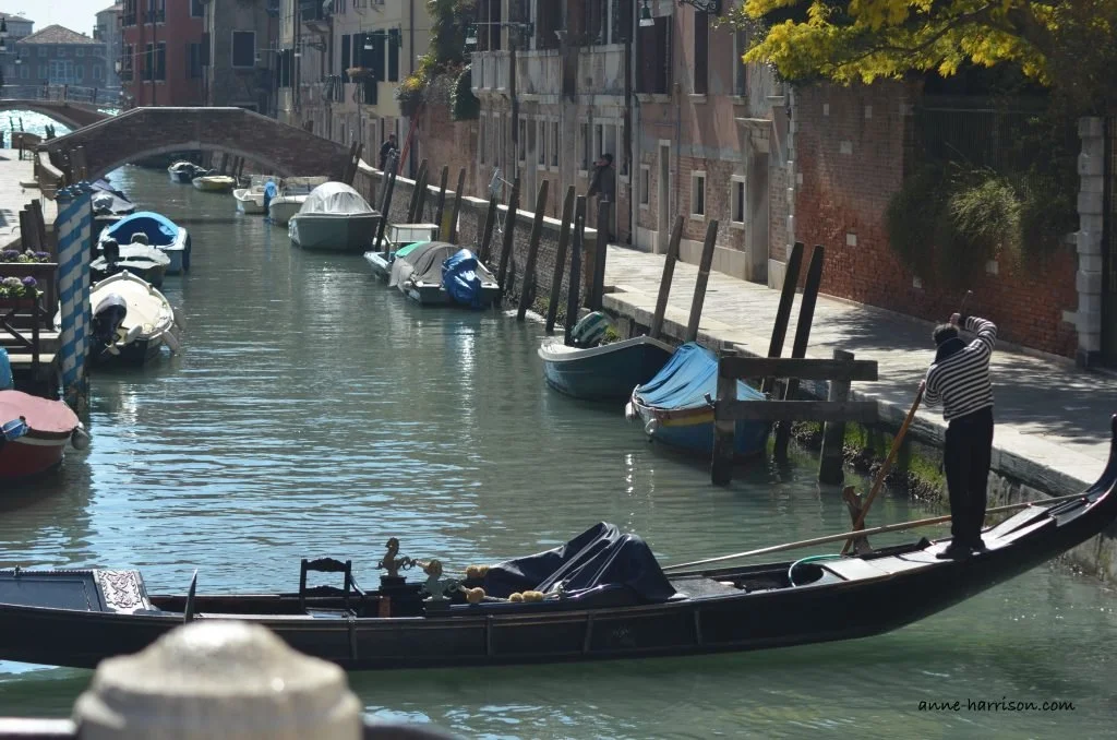 A gondola turning around in a narrow canal. The gondola is horizontal, and almost touching both sides of the canal