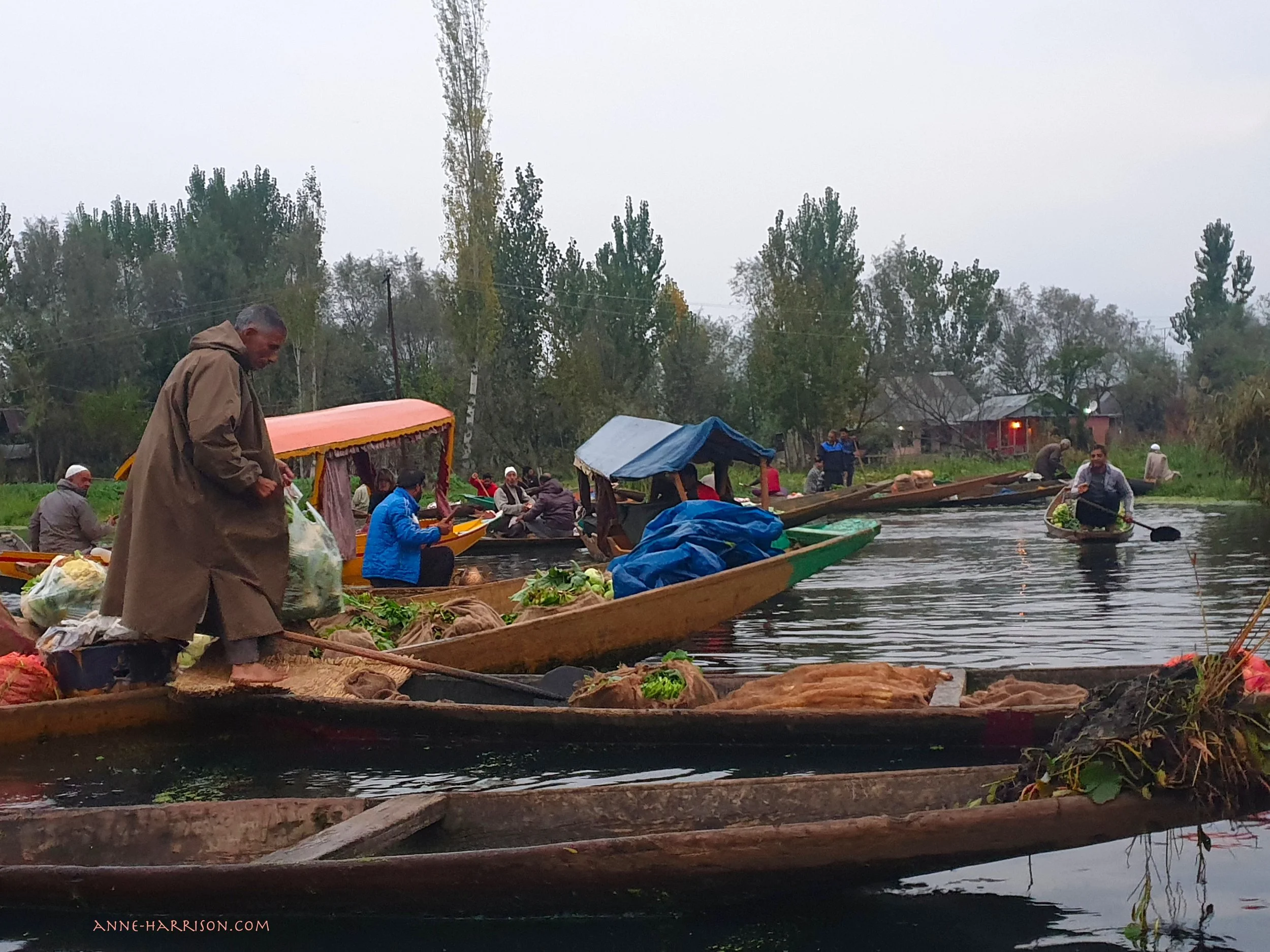 Men standing and paddling wooden long boats in a floating market in India
