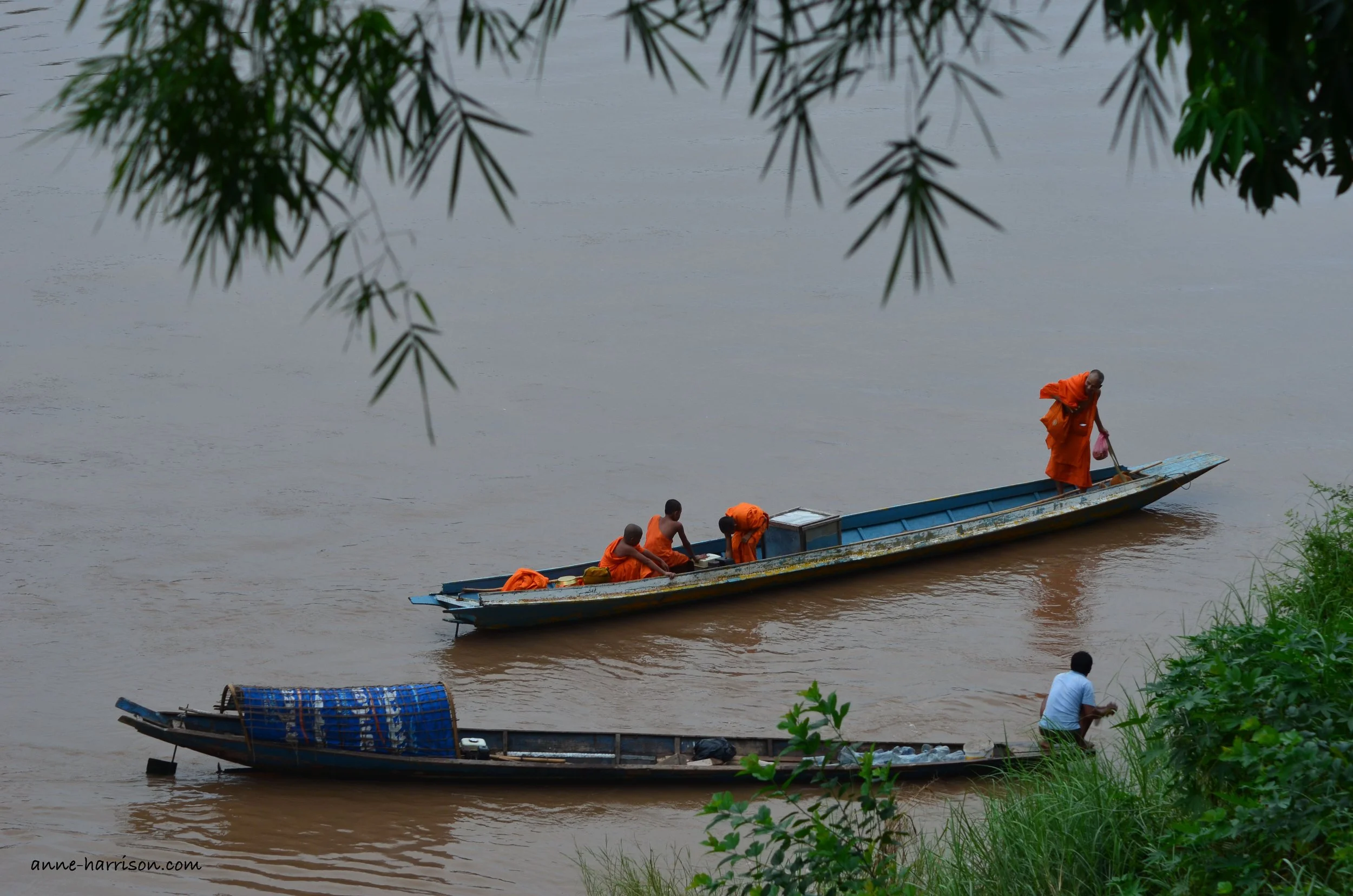 Monks in orang robes crossing a river in a longboat in Laos