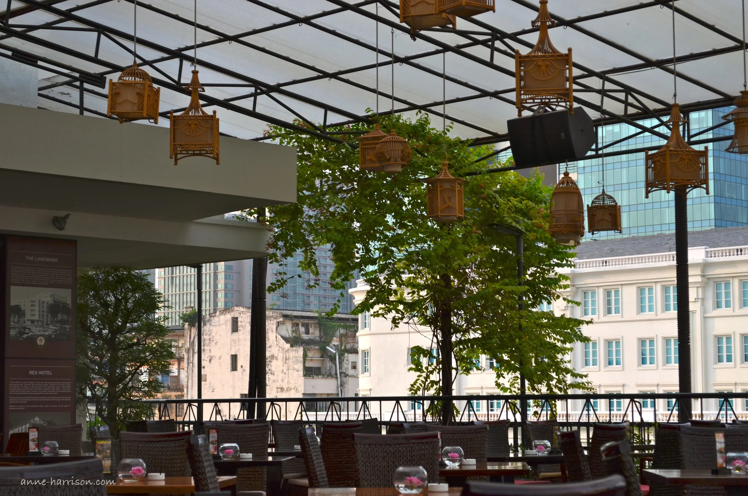 Wooden lanterns hang from the ceiling of a rooftop bar in Saigon, Vietnam. Vases with a pink floating flower isareon every table
