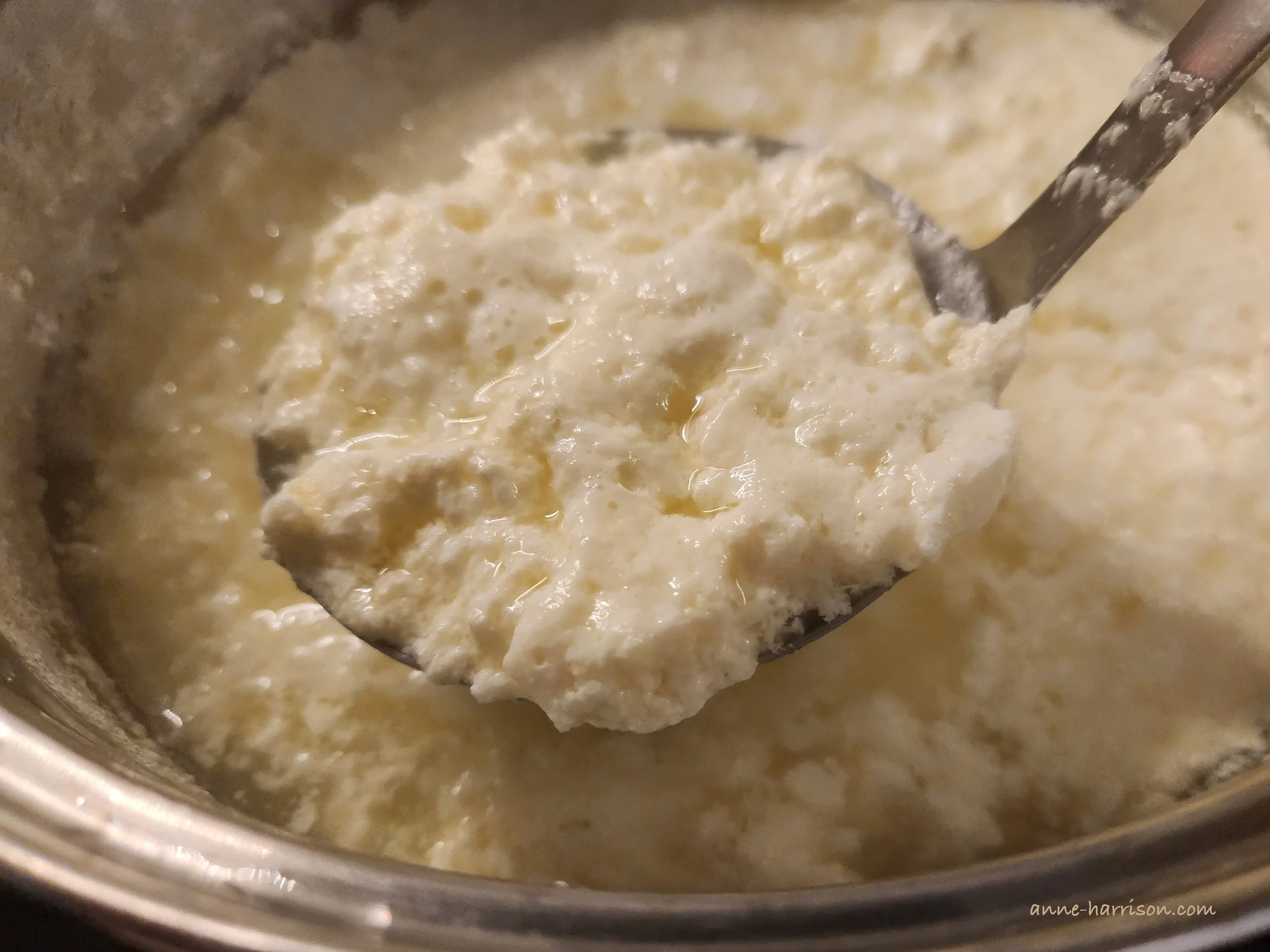 A slotted spoon transferring curdled tofu from a pot.
