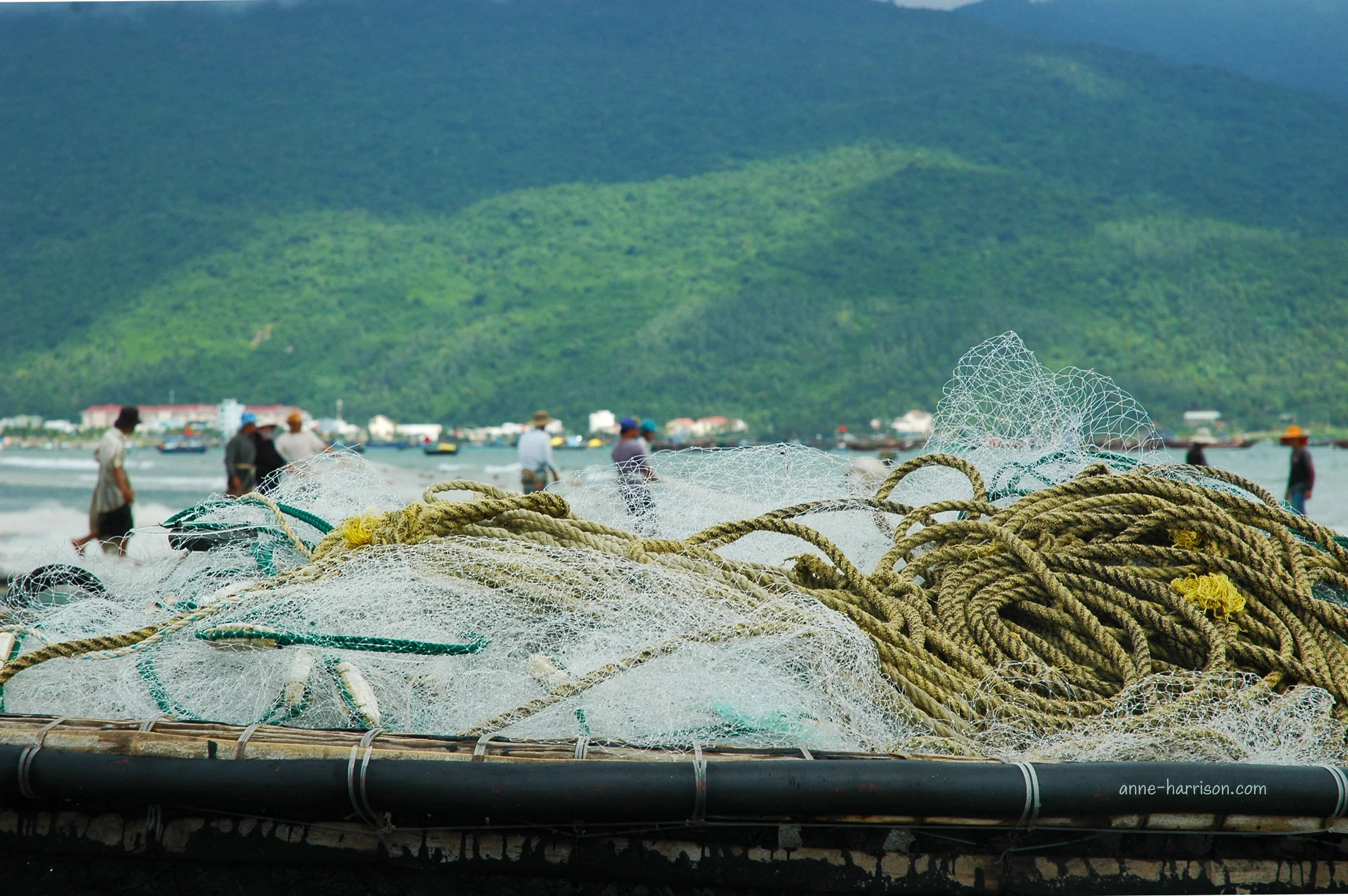 Fishing nets and rope are piled onto a round basket boat in Vietnam. Fishermen pulling on nets are just visible in the background.