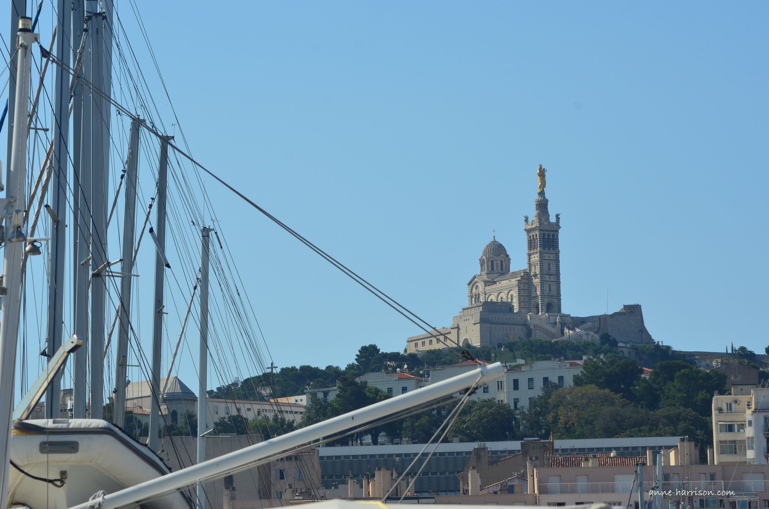 Masts and rigging frame a view of Marseille's Basilica de la Notre Dame de la Garde.
