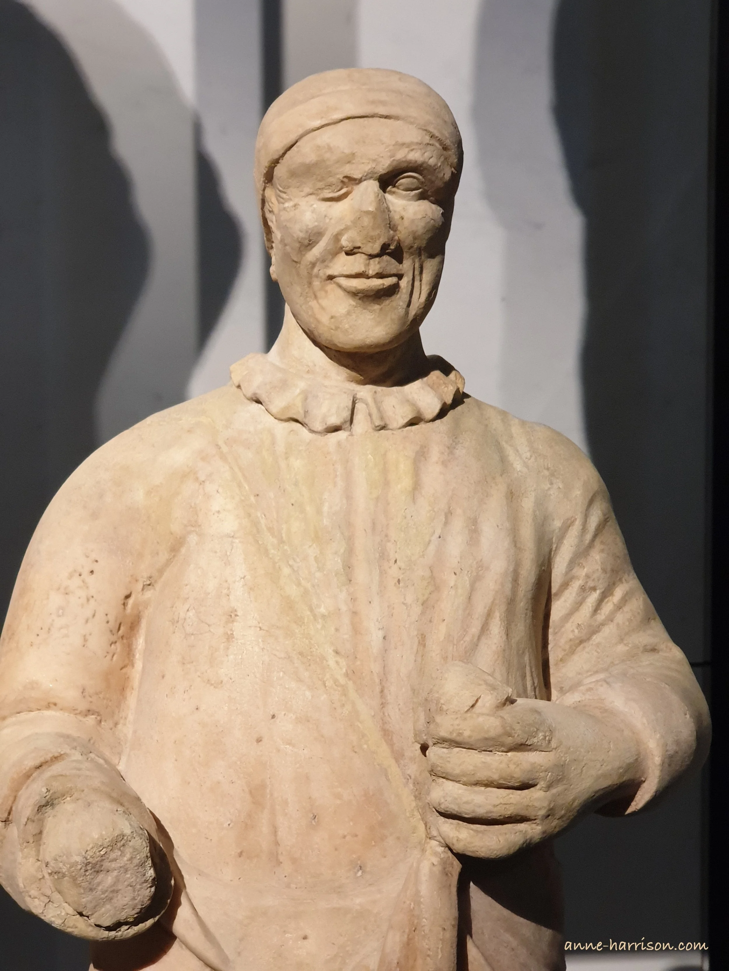 A damaged scuplture of a man with a cap and a high-necked shirt sith a frill. One hand a his nose a missing.