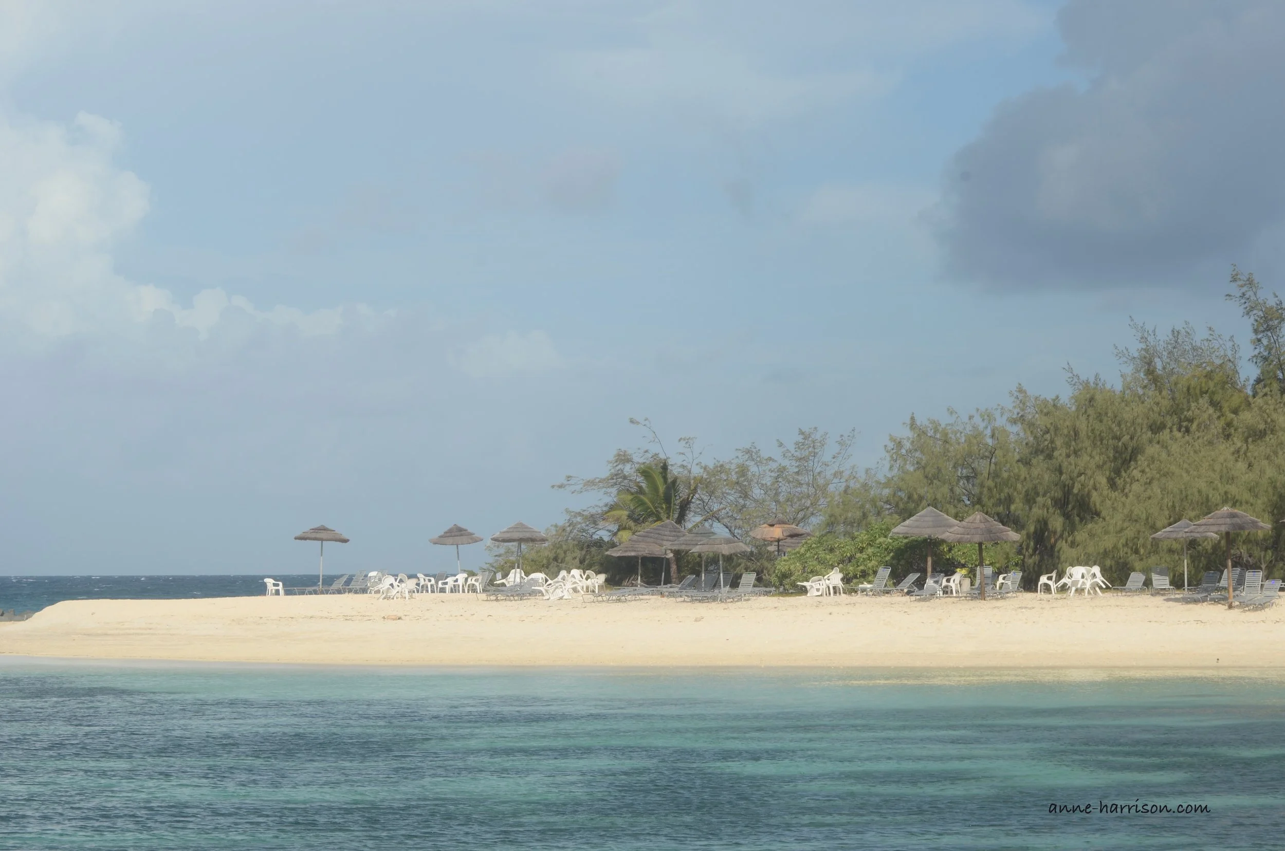 Plastic white chairs and thatch beach umbrellas on the sand of a tropical island.
