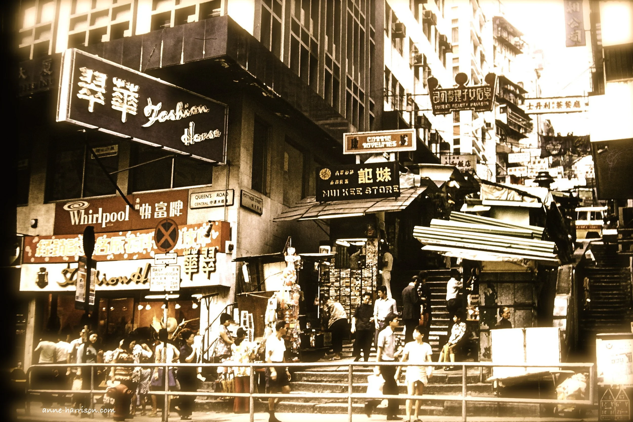 An old sepia photo of Queen's Road and Pottinger Street in Hong Kong. Te streets are crowded and filled with signs in English and Cantonese, and stalls line the steps of Pottinger street, and Pottin