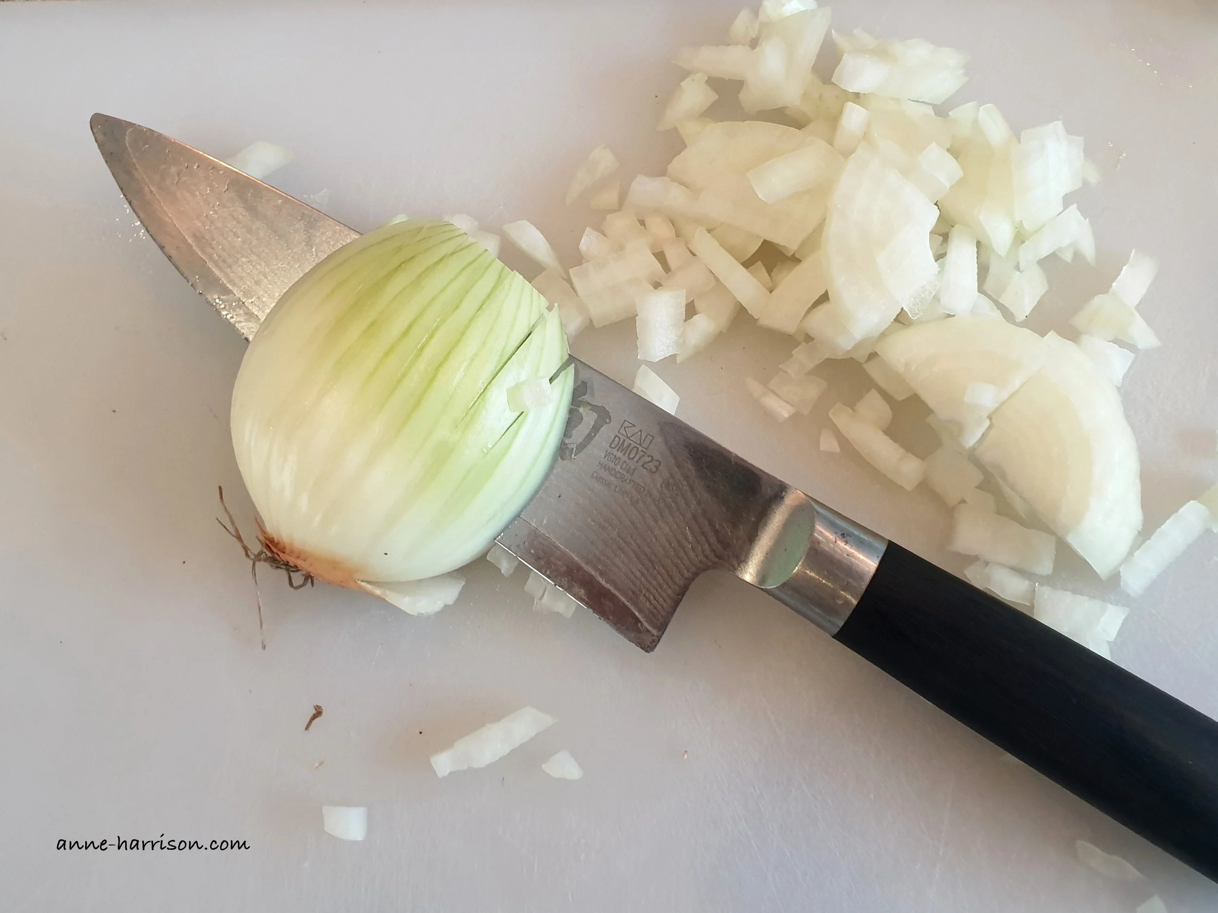 A knife is resting inside a partially sliced white onion. Beside it is a pile of diced onion.