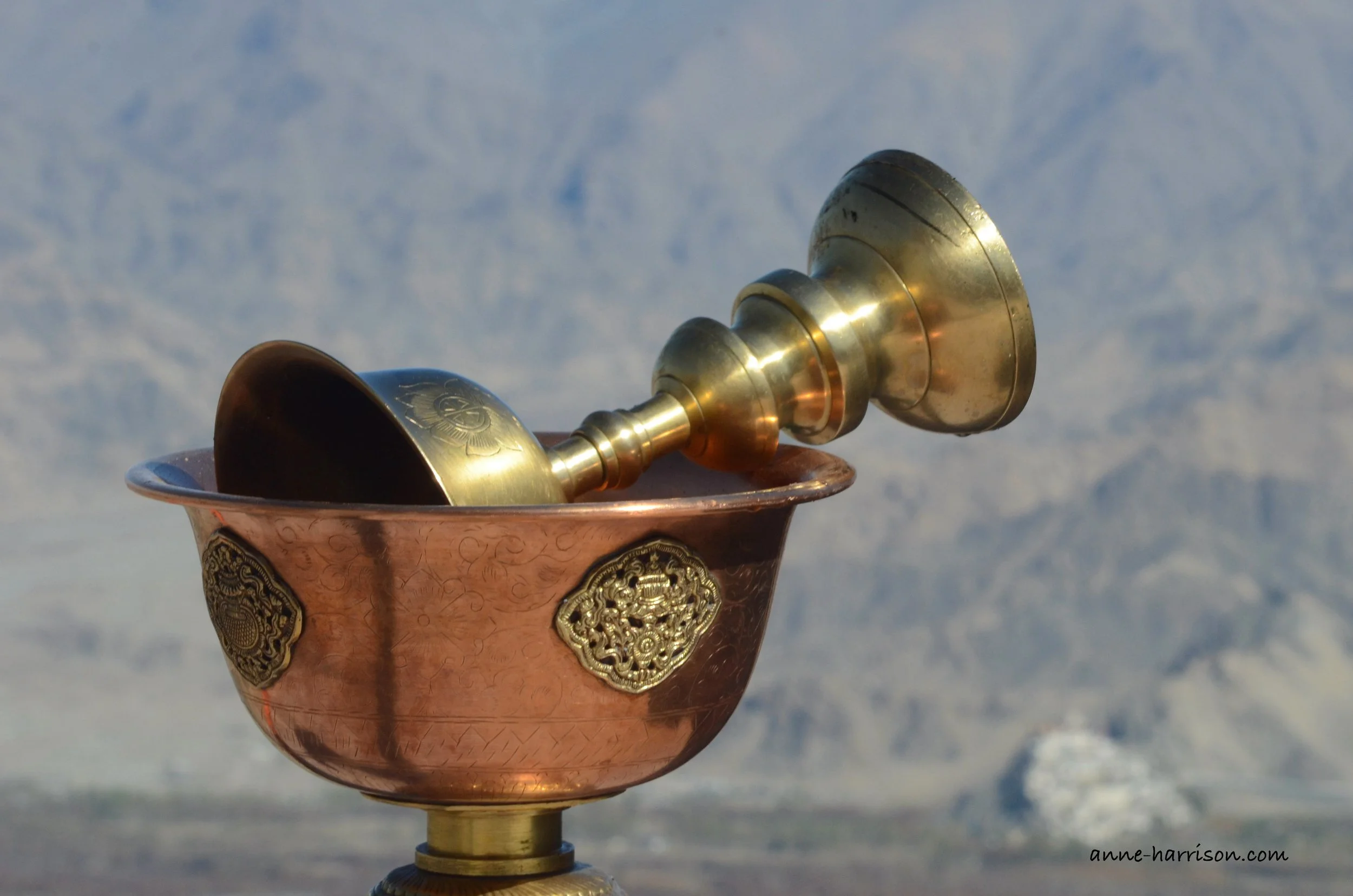 a bronze cup and bowl used as part of a religious ceremony, seen against a backdrop of mountains