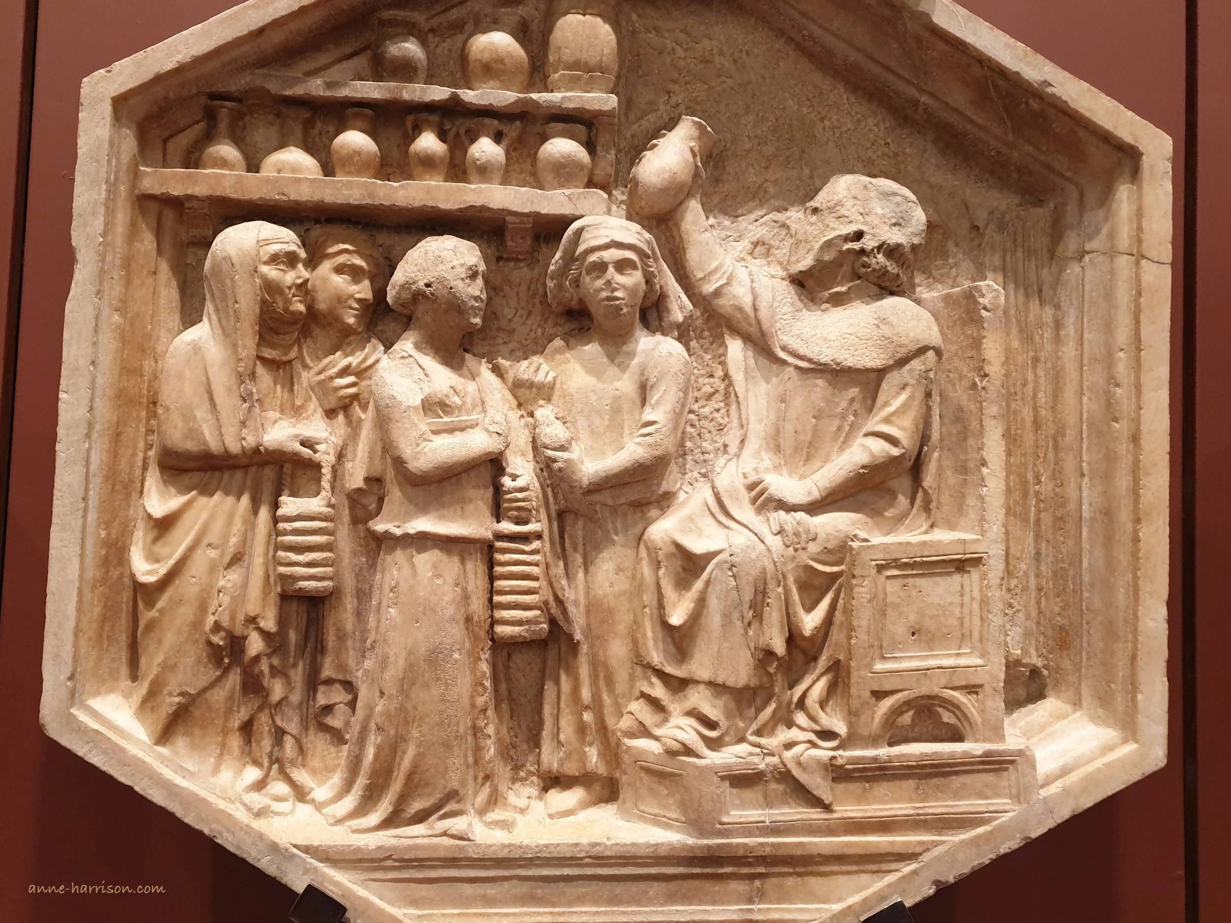 A Renaissance relief carving showing a doctor sitting and holding a flask up to be examined. In front of him are 4 patients, and shelves containing vials.