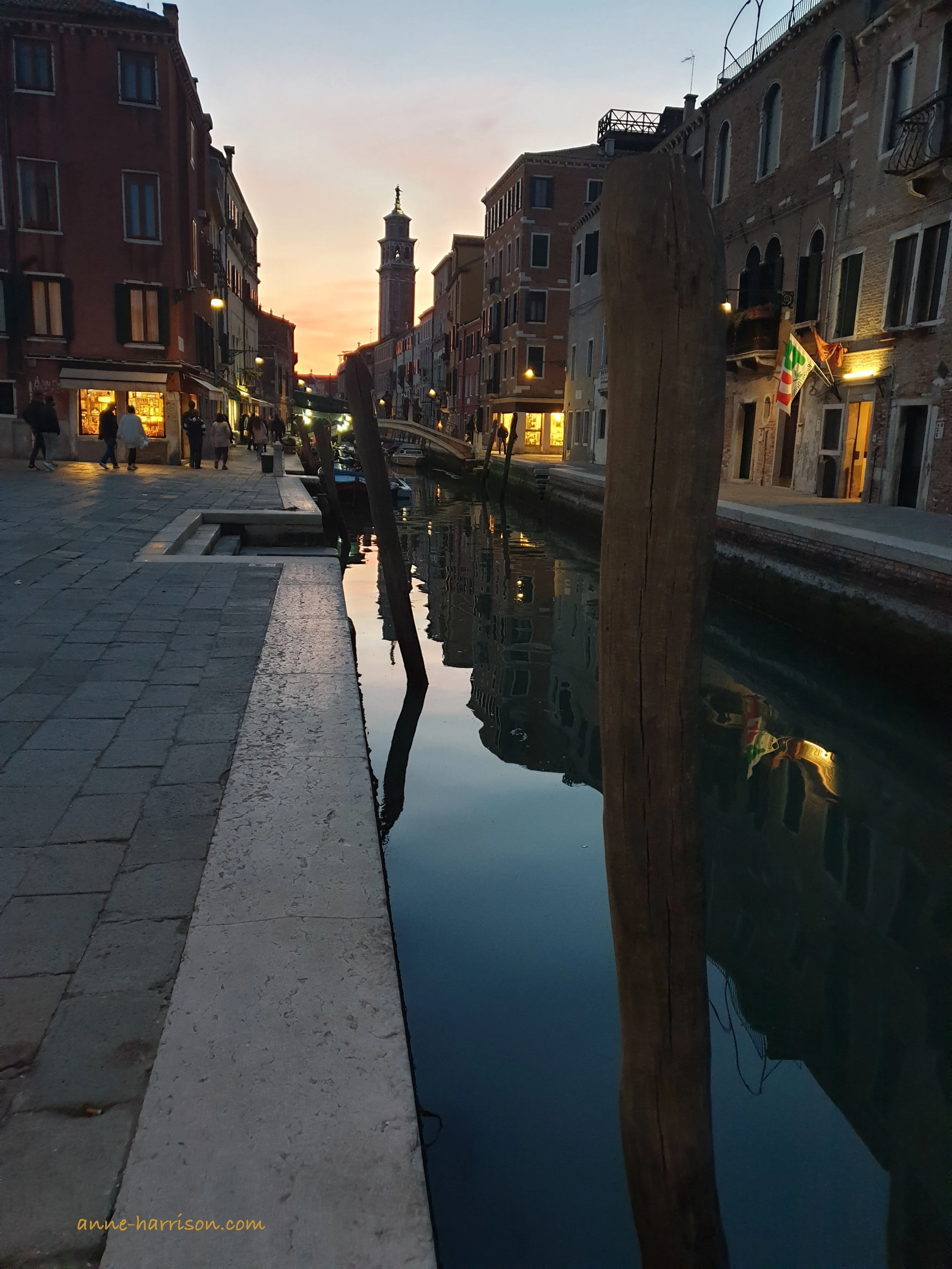 The Rio San Barnaba, a canal in venice, seen at night, from ground level. The buildings and lights are reflected in the still water.