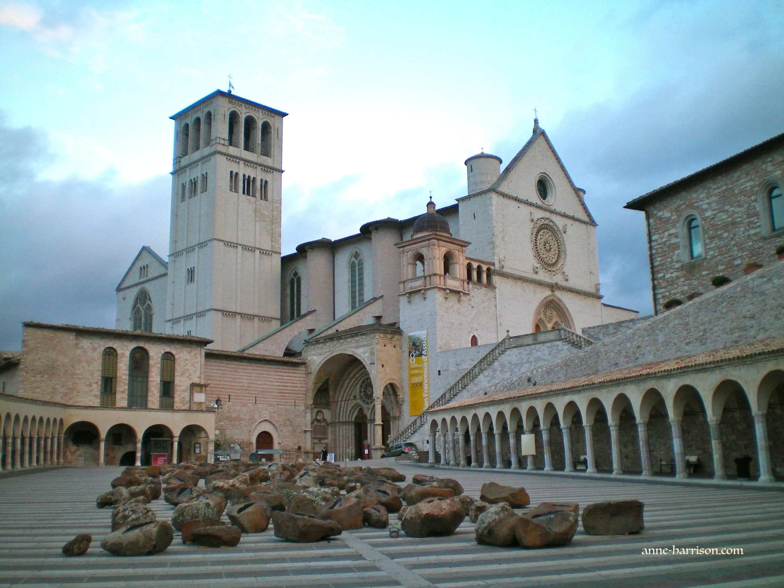 The lower courtyard outside the Basilica of St Francis of Assisi. It is filled with large stones. The sky is ovecast.