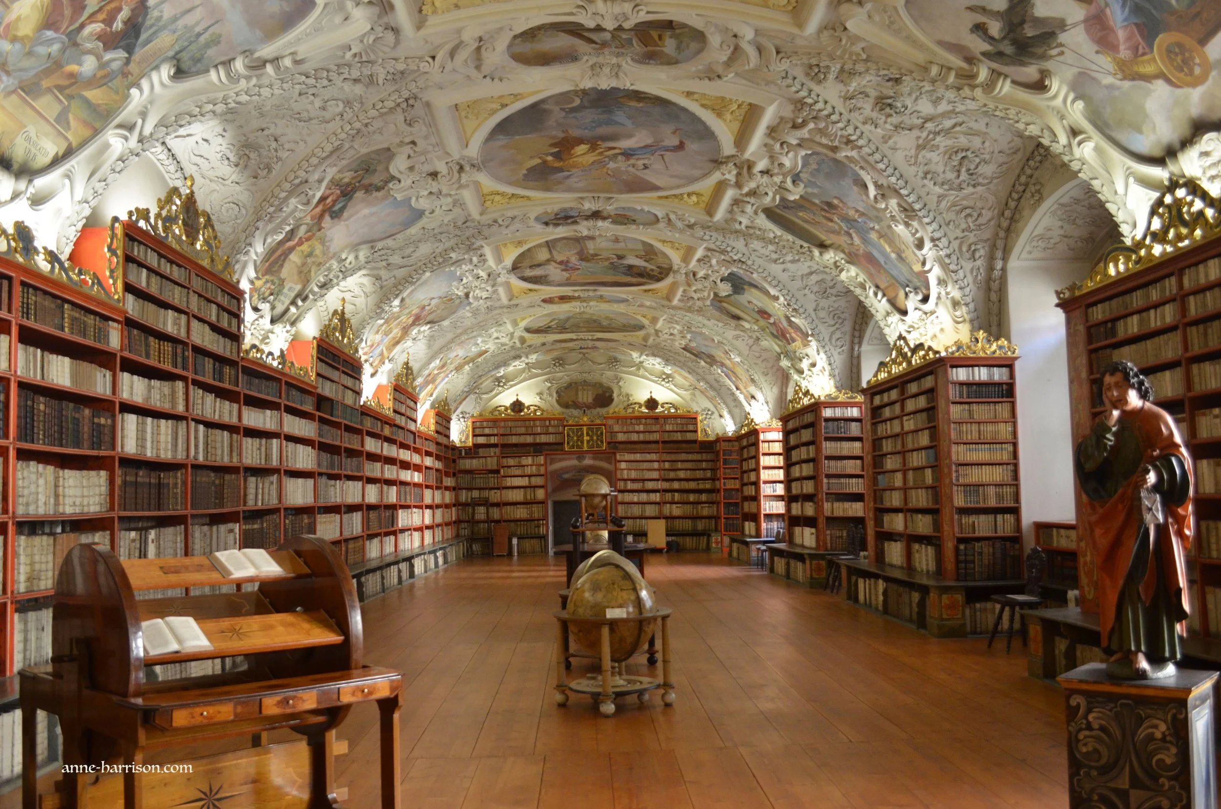 A libraey with talk bookcases, a roof covered in frescoes, a desk in the foreground and a wooden globe.
