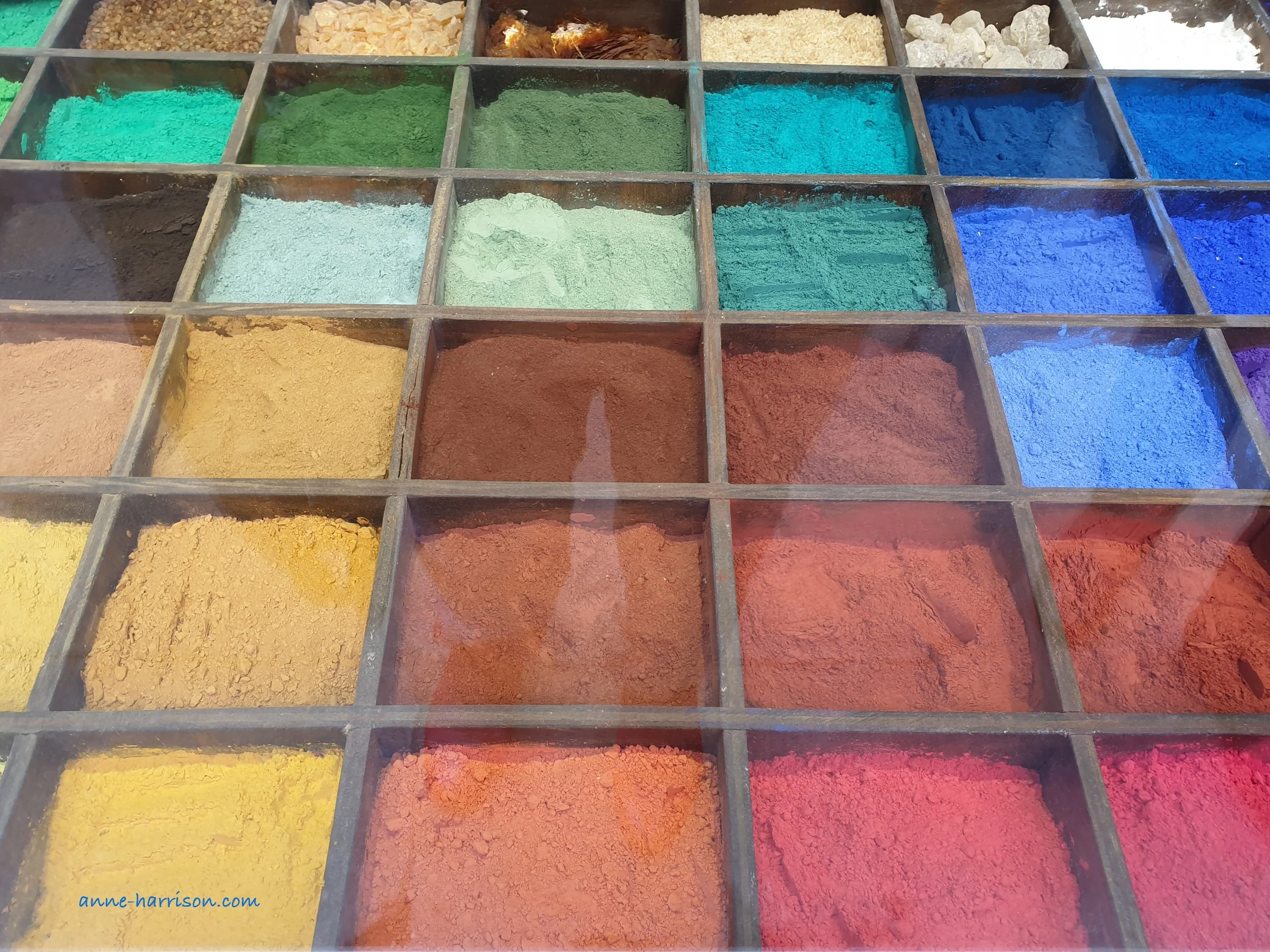 A wooden box divided into segments filled with ground paint pigment of all colours.