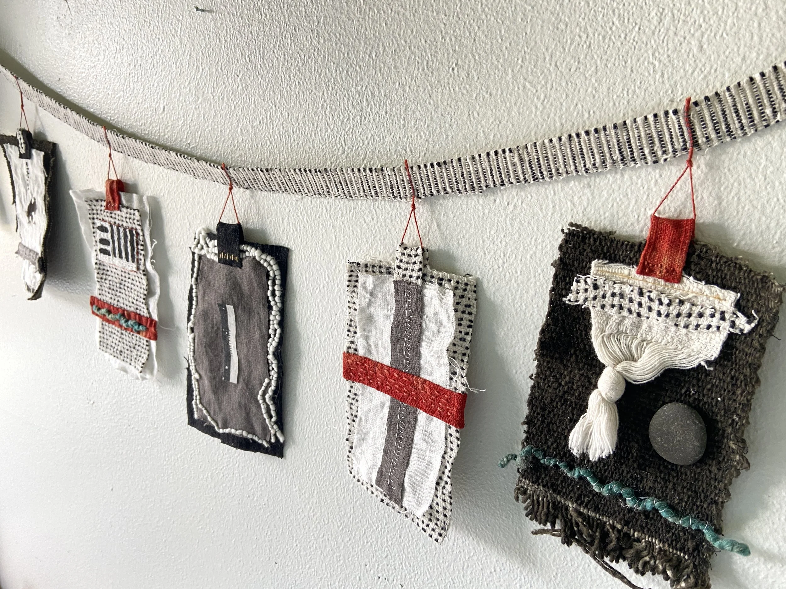 Mixed media wabi sabi prayer flags created by Emma Freeman in Wisconsin using repurposed fabric, textiles, found nature, slow stitching, and hand embroidery, mark making, abstract art compositions and expressions, black, white, red and grey prayer fl