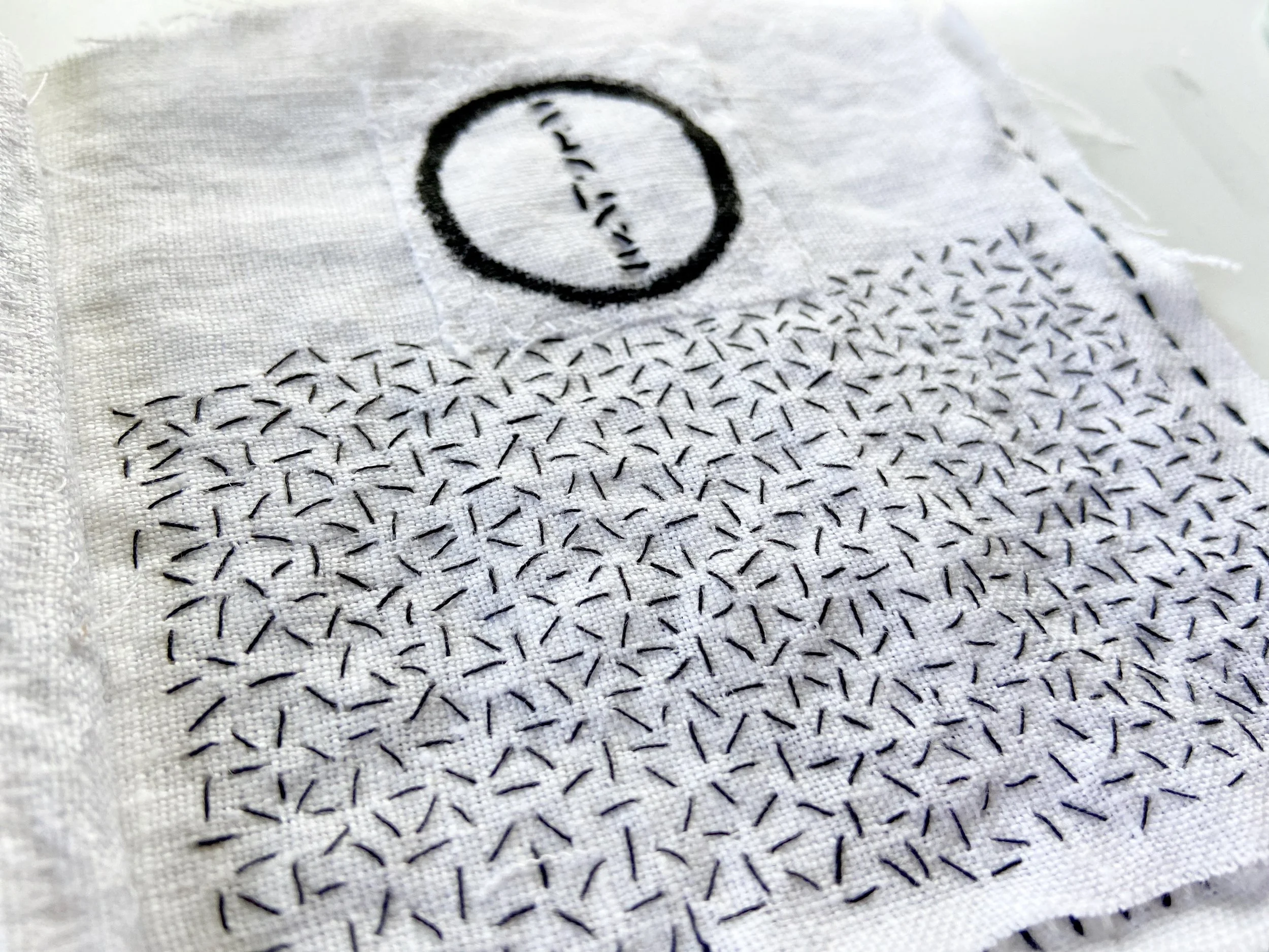 Black and white textile meditation book with ensō circle painting on white linen and slow, hand stitching seed stitch made by Emma Freeman, contemplative mixed media artist and teaching artist in Wisconsin. Hand painted textiles, textile artist, fabr