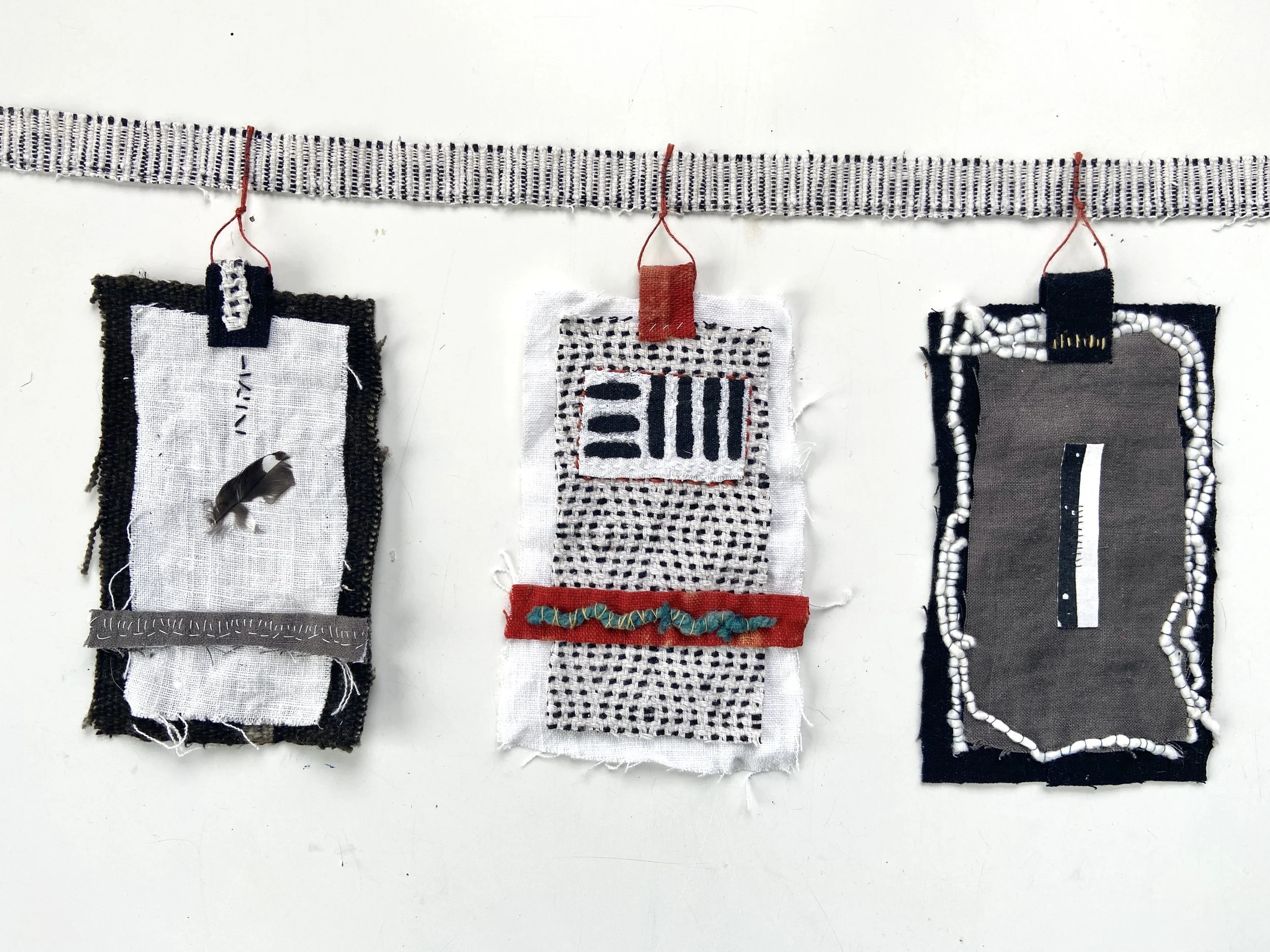 Mixed media wabi sabi prayer flags created by Emma Freeman in Wisconsin using repurposed fabric, textiles, found nature, slow stitching, and hand embroidery, mark making, abstract art compositions and expressions, black, white, red and grey prayer fl