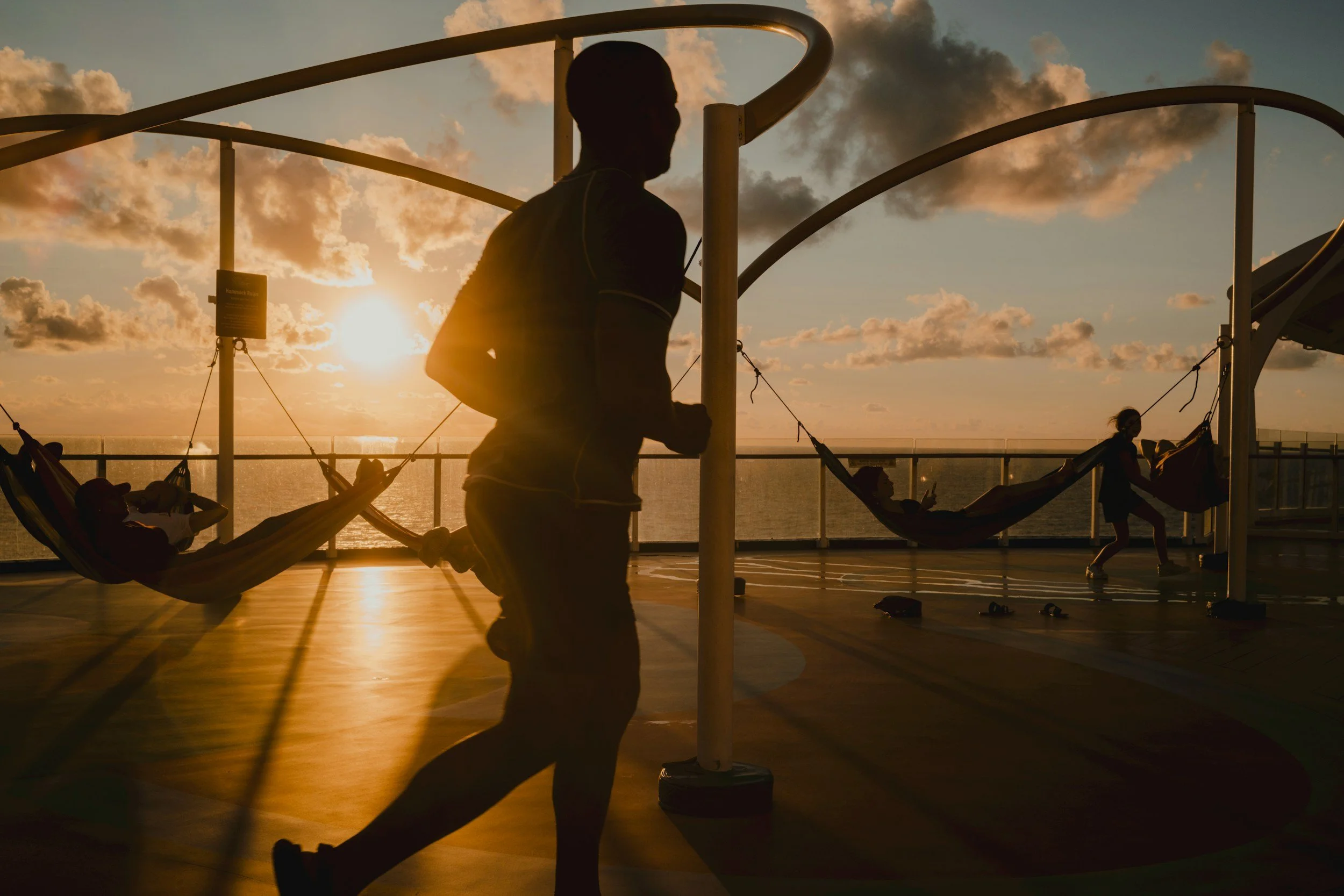 Silhouette of a person jogging on a luxury cruise ship deck at sunset.