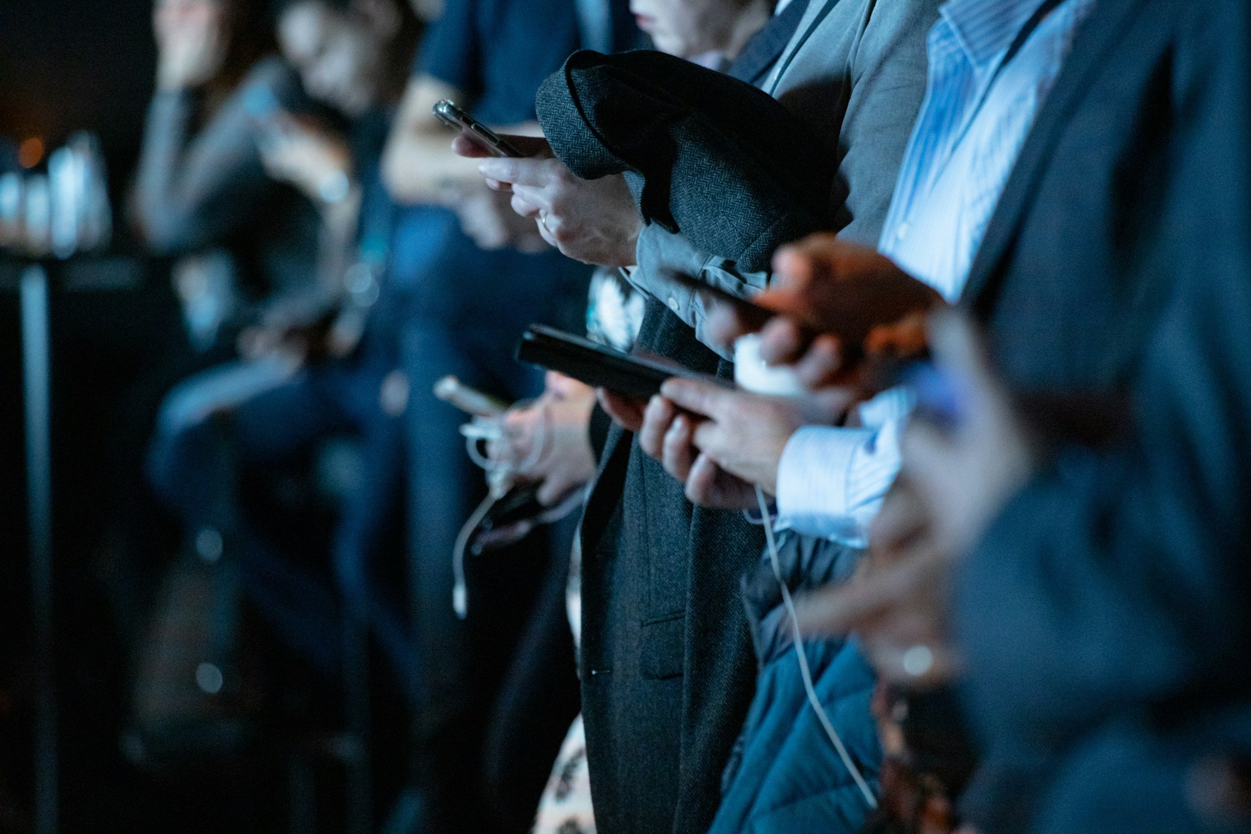 People sitting on chairs and using their smartphones in a conference or event setting.