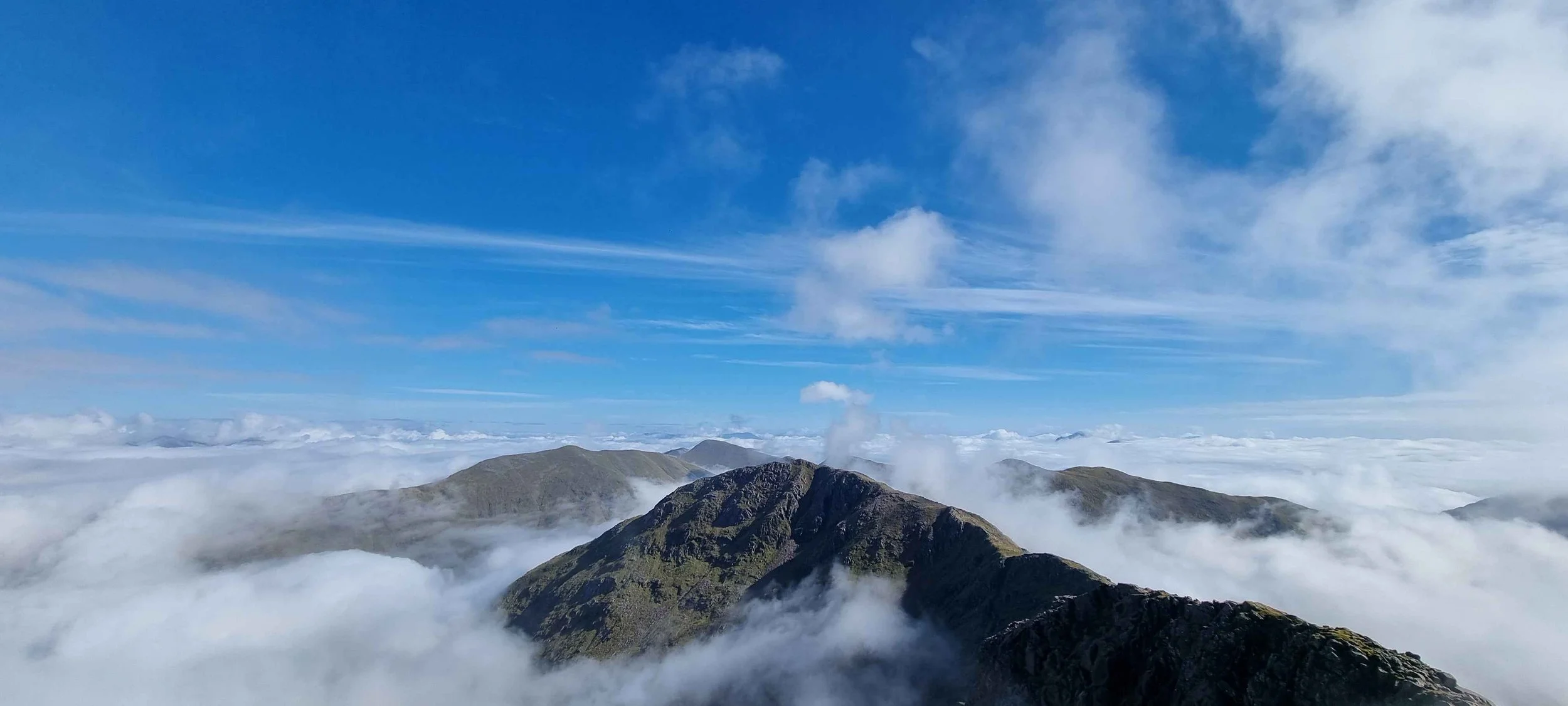 Mountain peaks above clouds with a blue sky and wispy clouds.