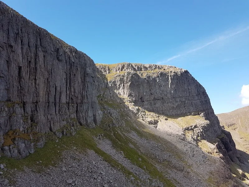 Cliffs and rocky hillside in a mountainous landscape under a clear blue sky.