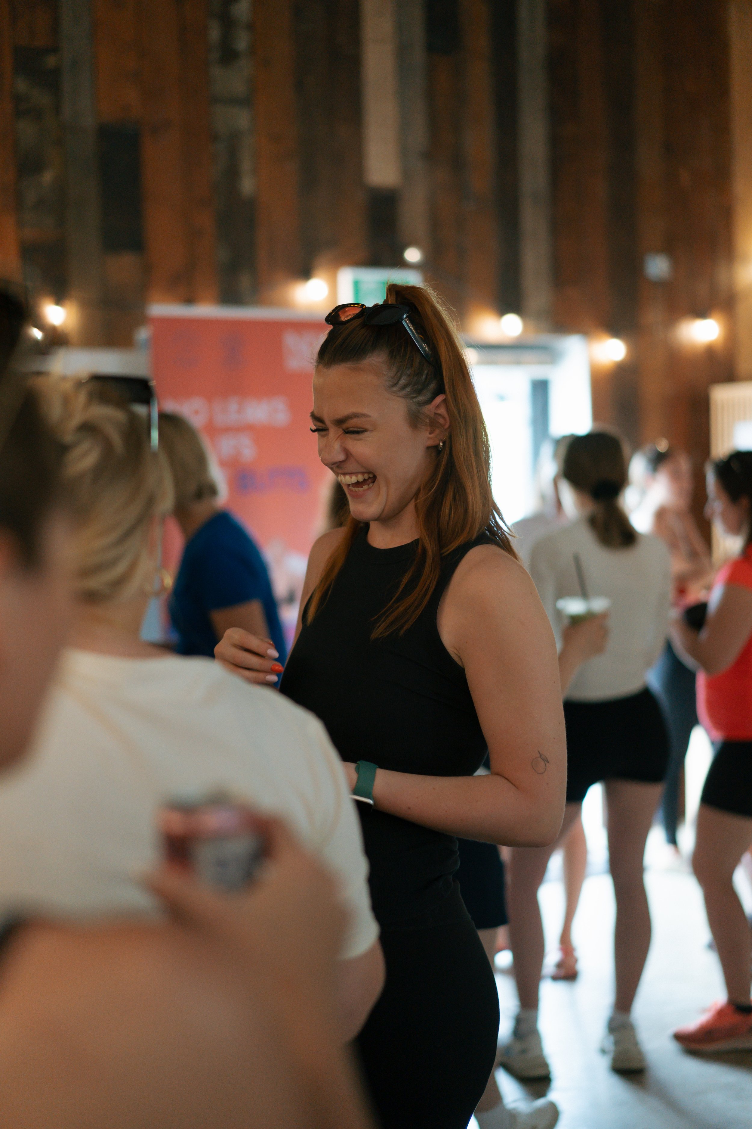 A woman with red hair laughing while socializing at an indoor event surrounded by other people.