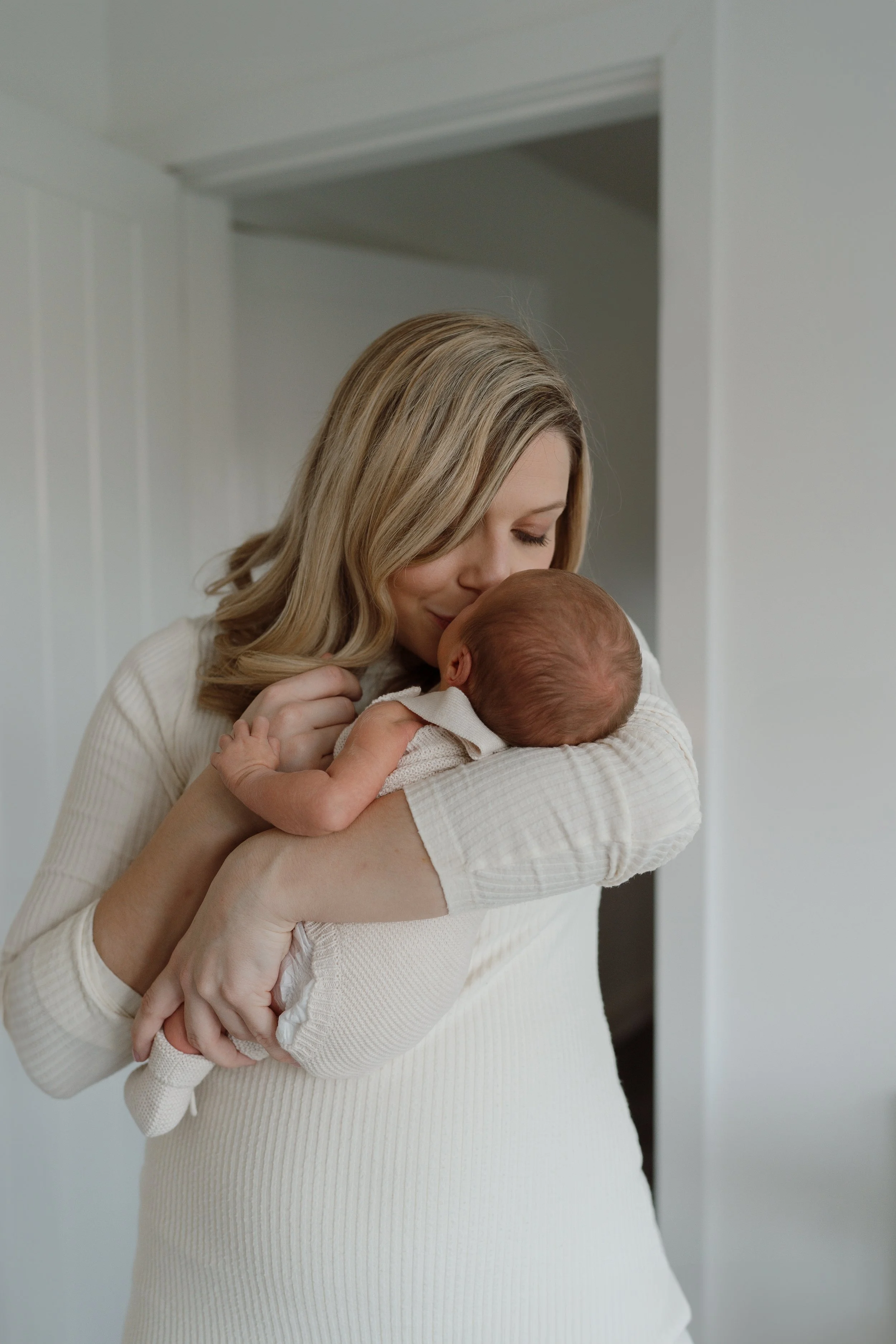 A woman holding a newborn baby close to her face, cuddling and kissing the baby's forehead.