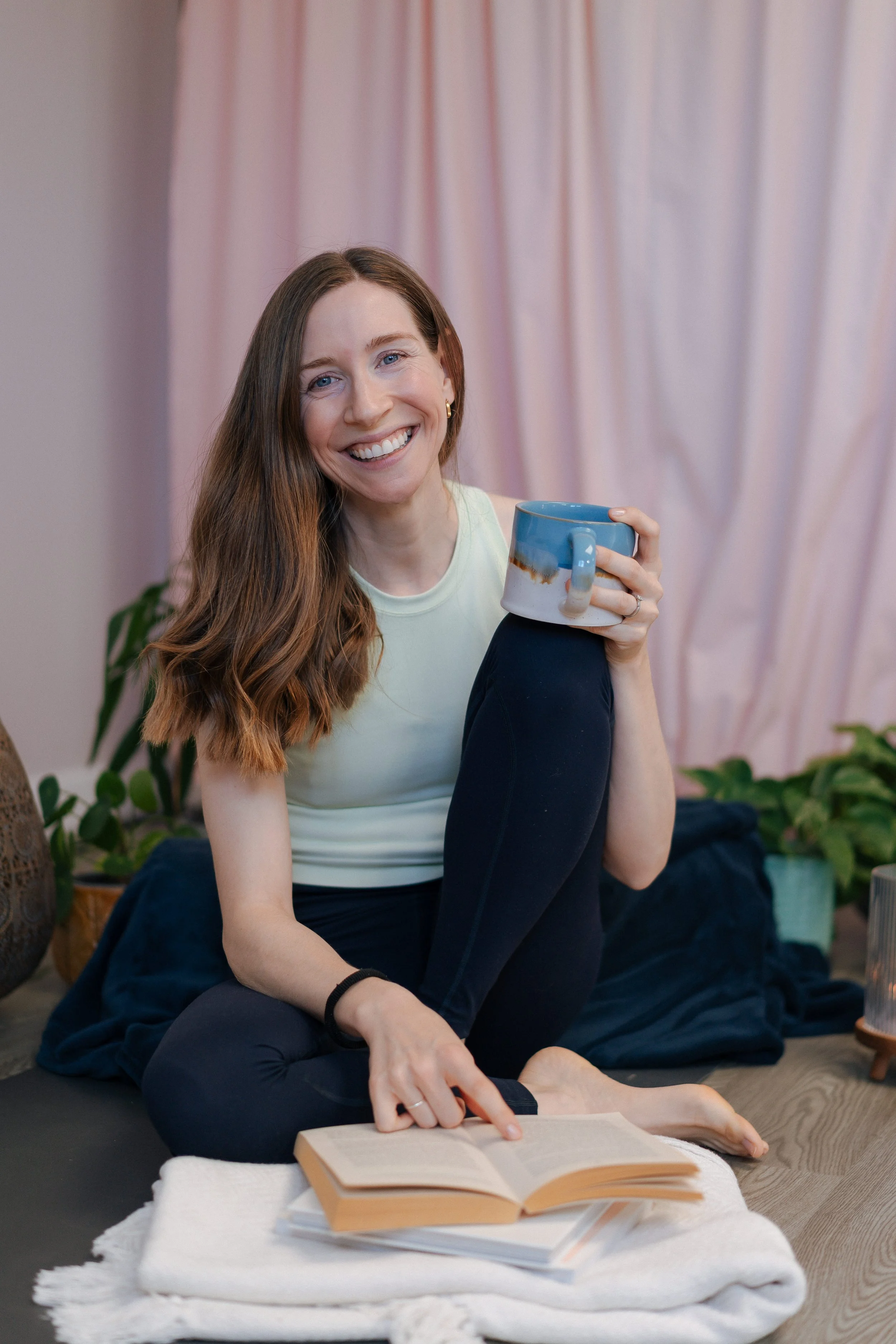 Wellness brand photography by Photography by Trish - woman sitting on the floor smiling with a book and mug, natural light personal brand session, Cambridge, UK