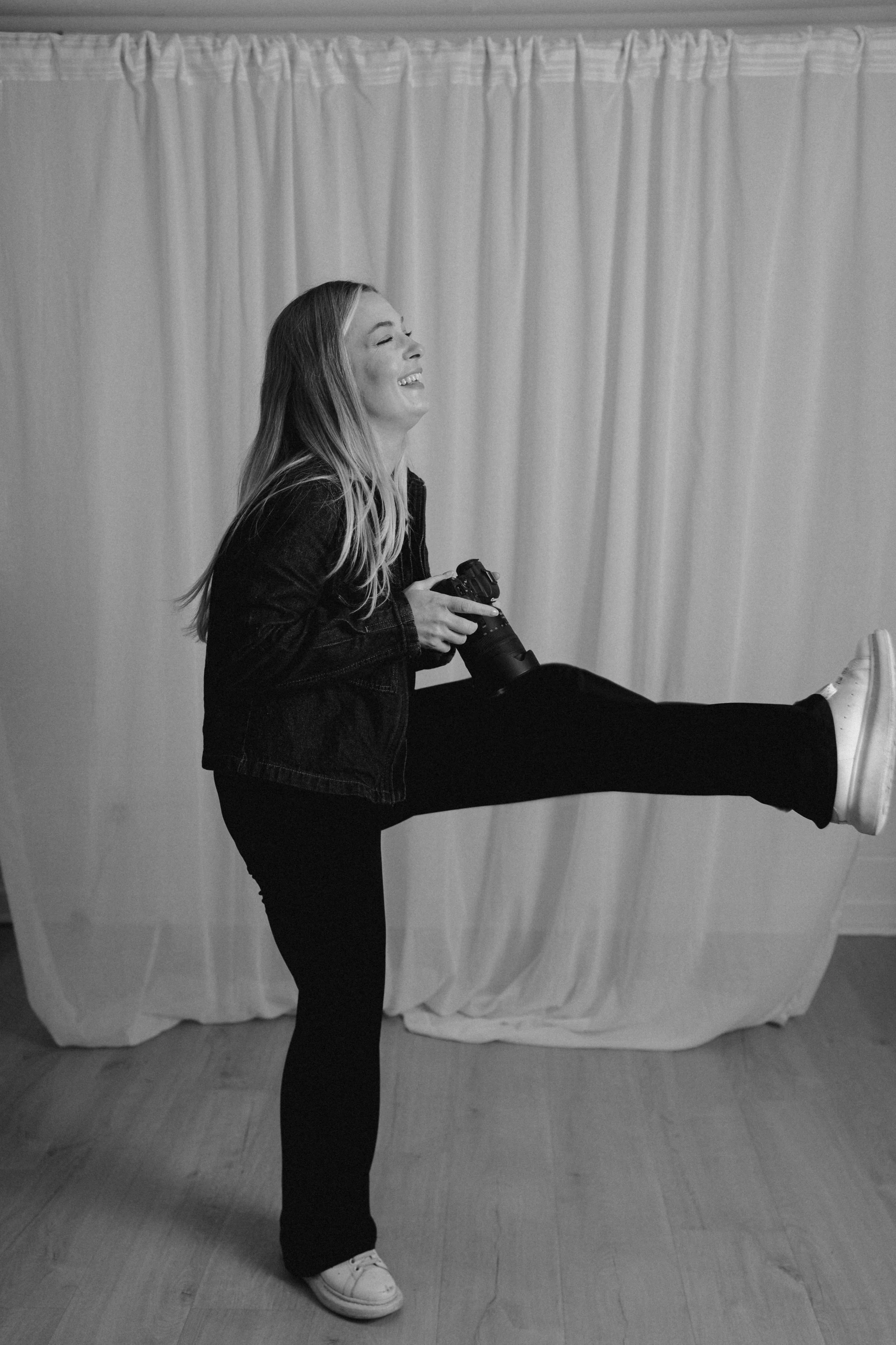 Brand photographer Cambridge - Trish from Photography by Trish laughing and kicking her leg up in a studio, fun and natural behind the scenes brand photography, UK