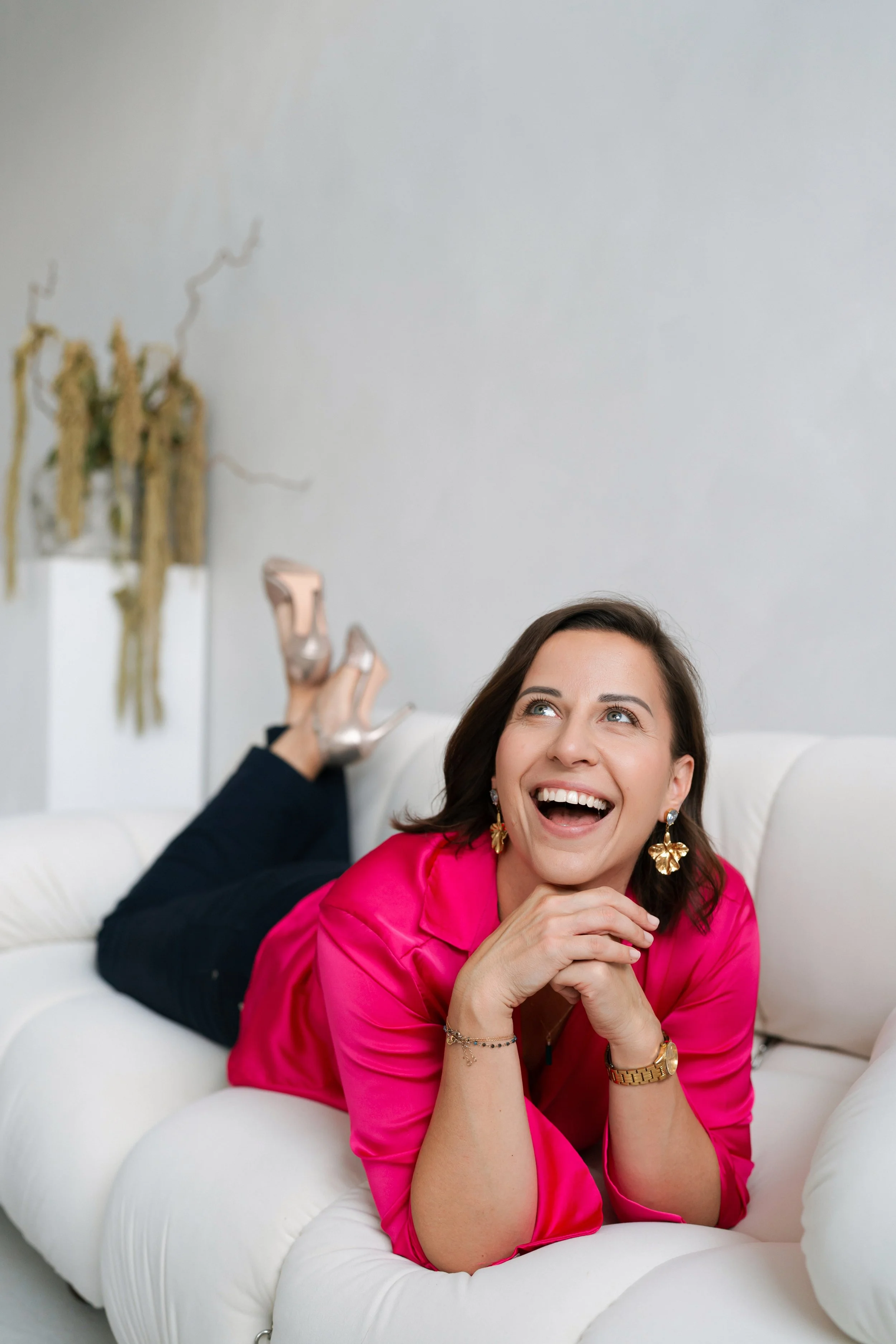 Personal brand photography by Photography by Trish - woman laughing joyfully in a pink blouse on a cream sofa, natural light brand session, Cambridge, UK