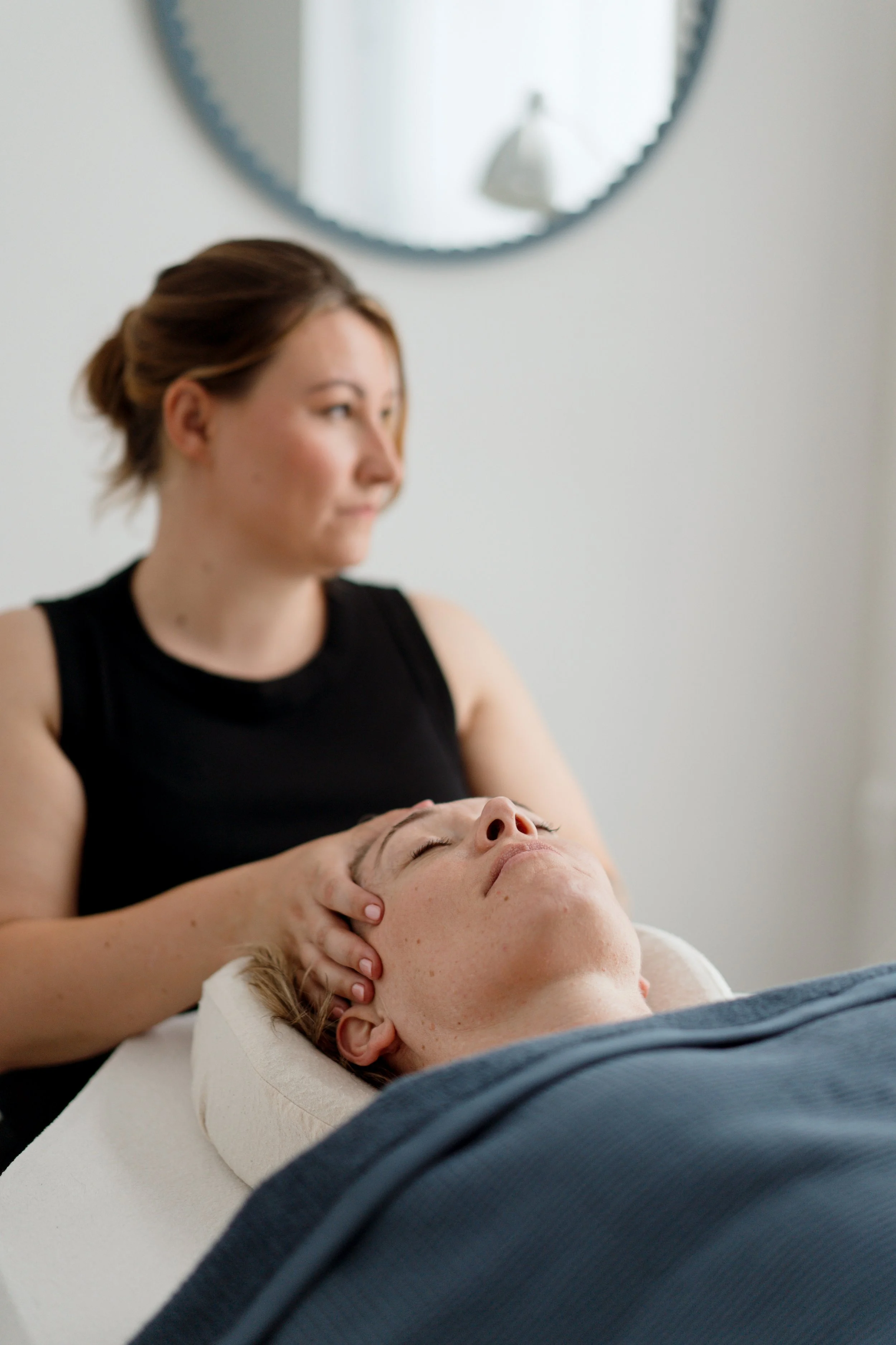A woman receiving a facial massage from a massage therapist in a spa room.