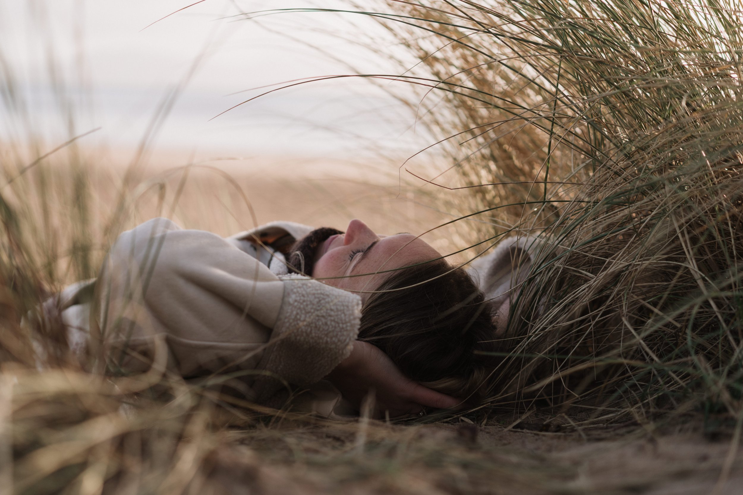 A woman lying on her back in a field of tall grass with her eyes closed and her hands behind her head.