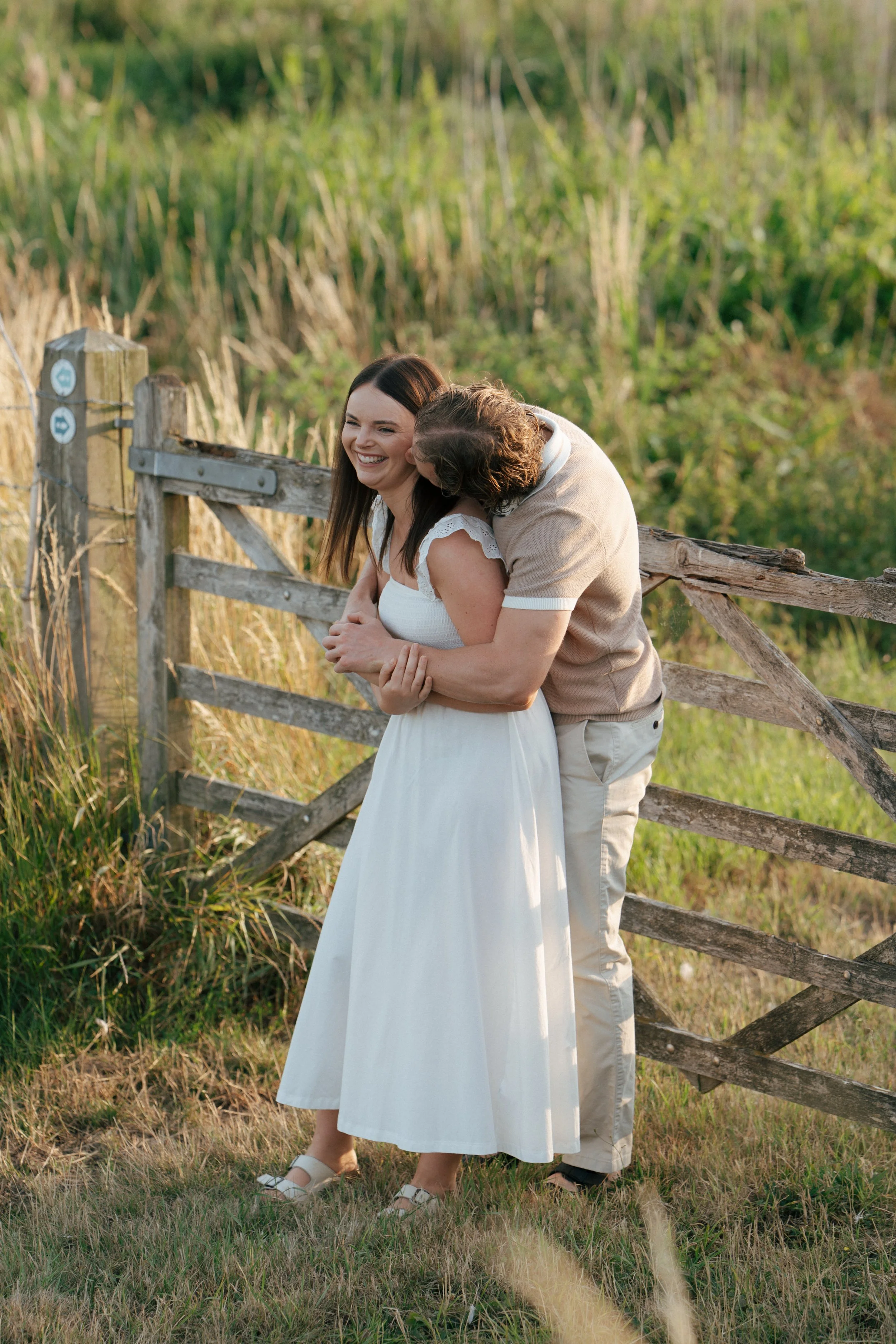 Two young boys sitting on a wooden bench outside near an autumn tree, smiling and enjoying the fall weather.