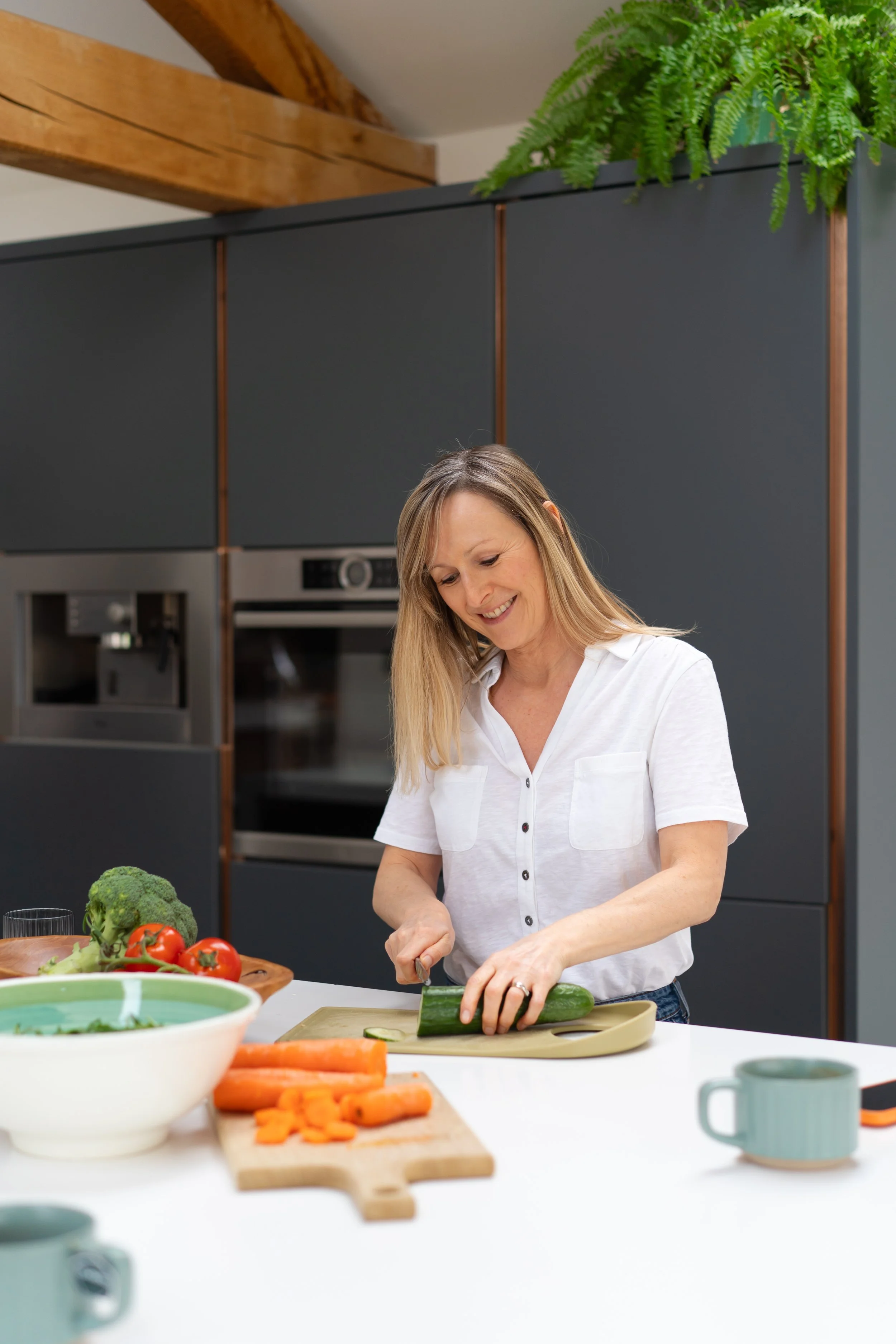 Woman chopping cucumber in a modern kitchen with vegetables and kitchenware on the counter