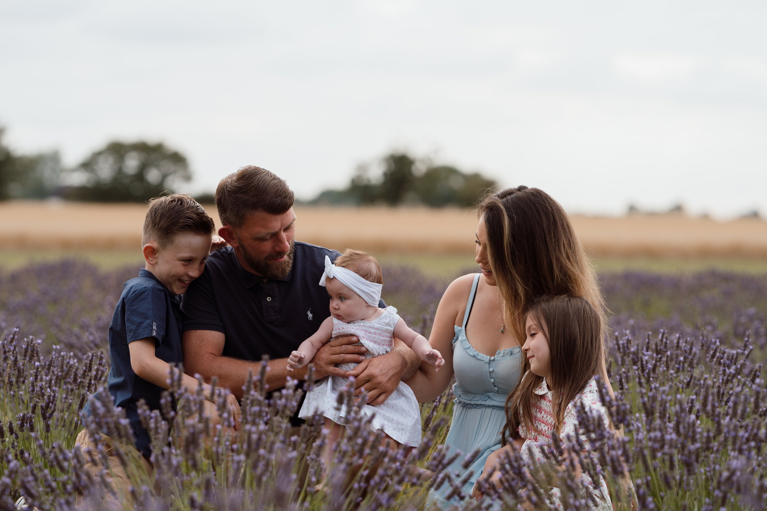 Family of five, including two children, in a lavender field during daytime, smiling and interacting with each other.