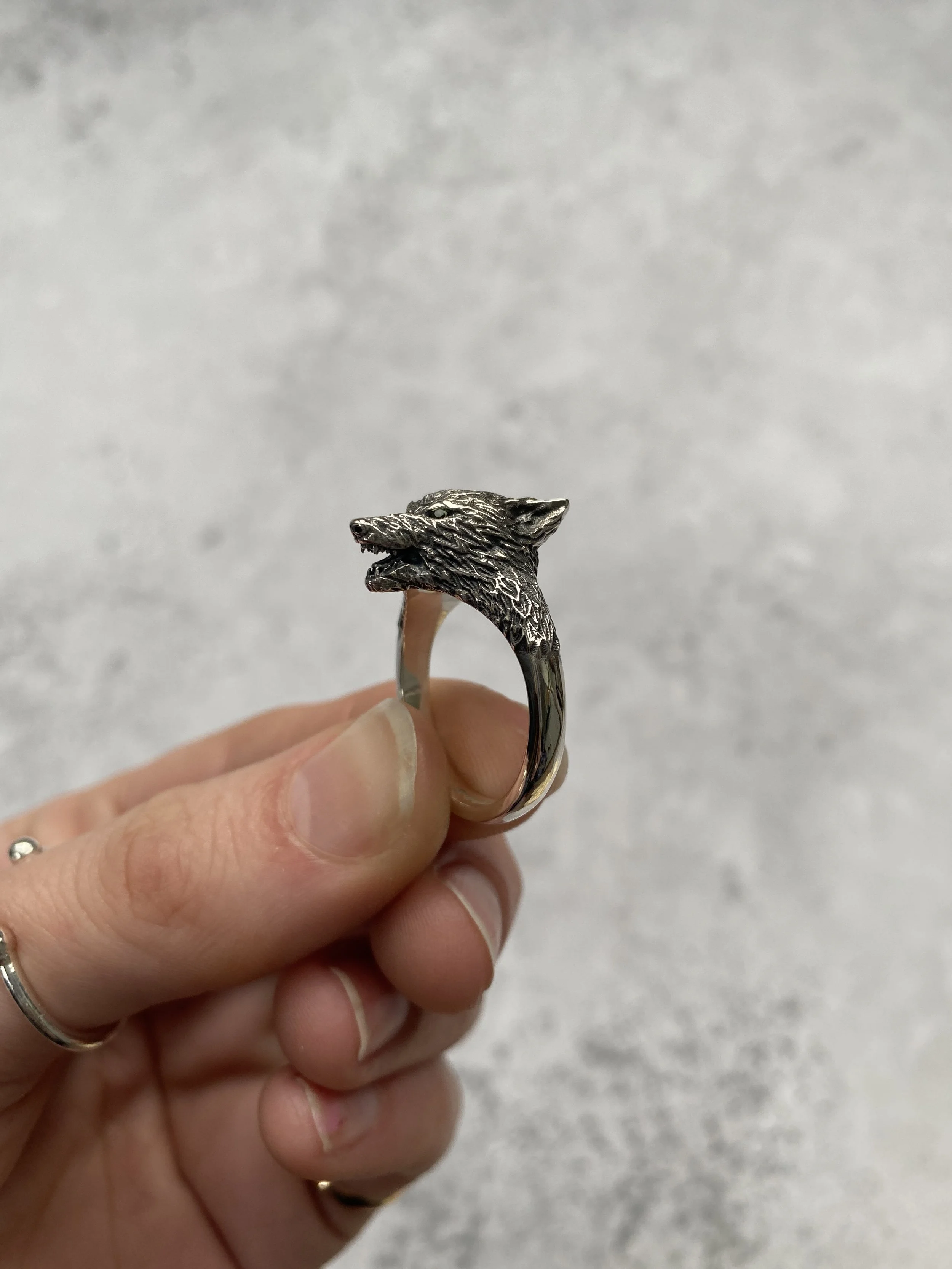 A person holding a silver ring with a wolf's head design on top.