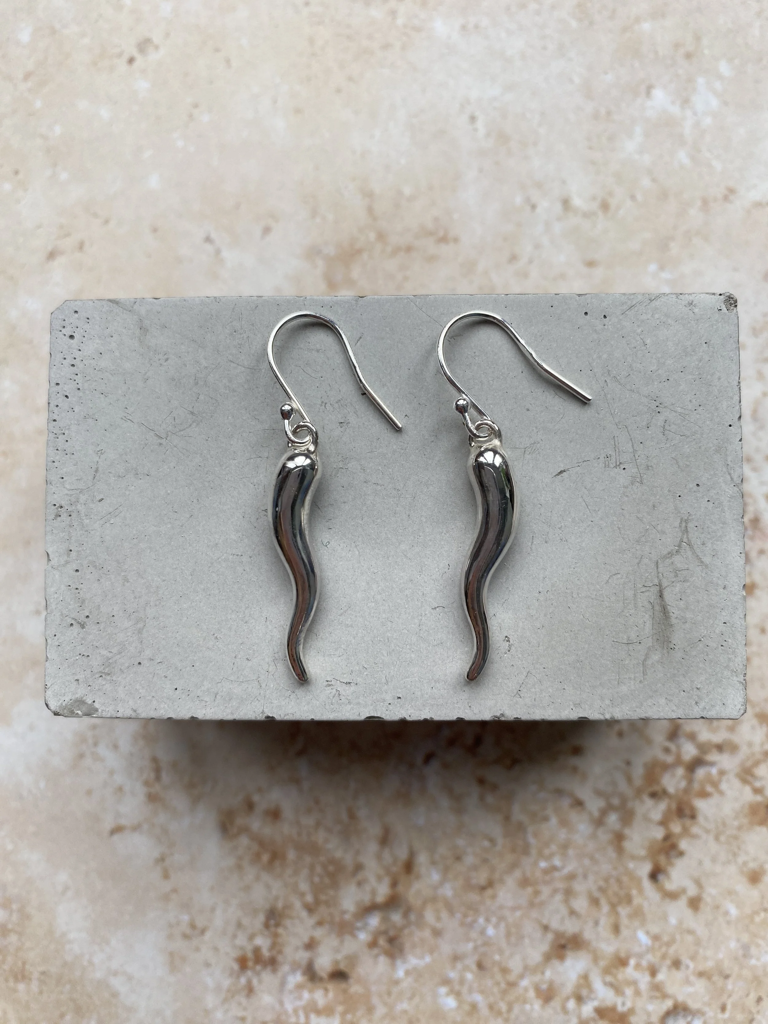 A pair of silver wavy-shaped dangling earrings displayed on a gray rectangular surface.