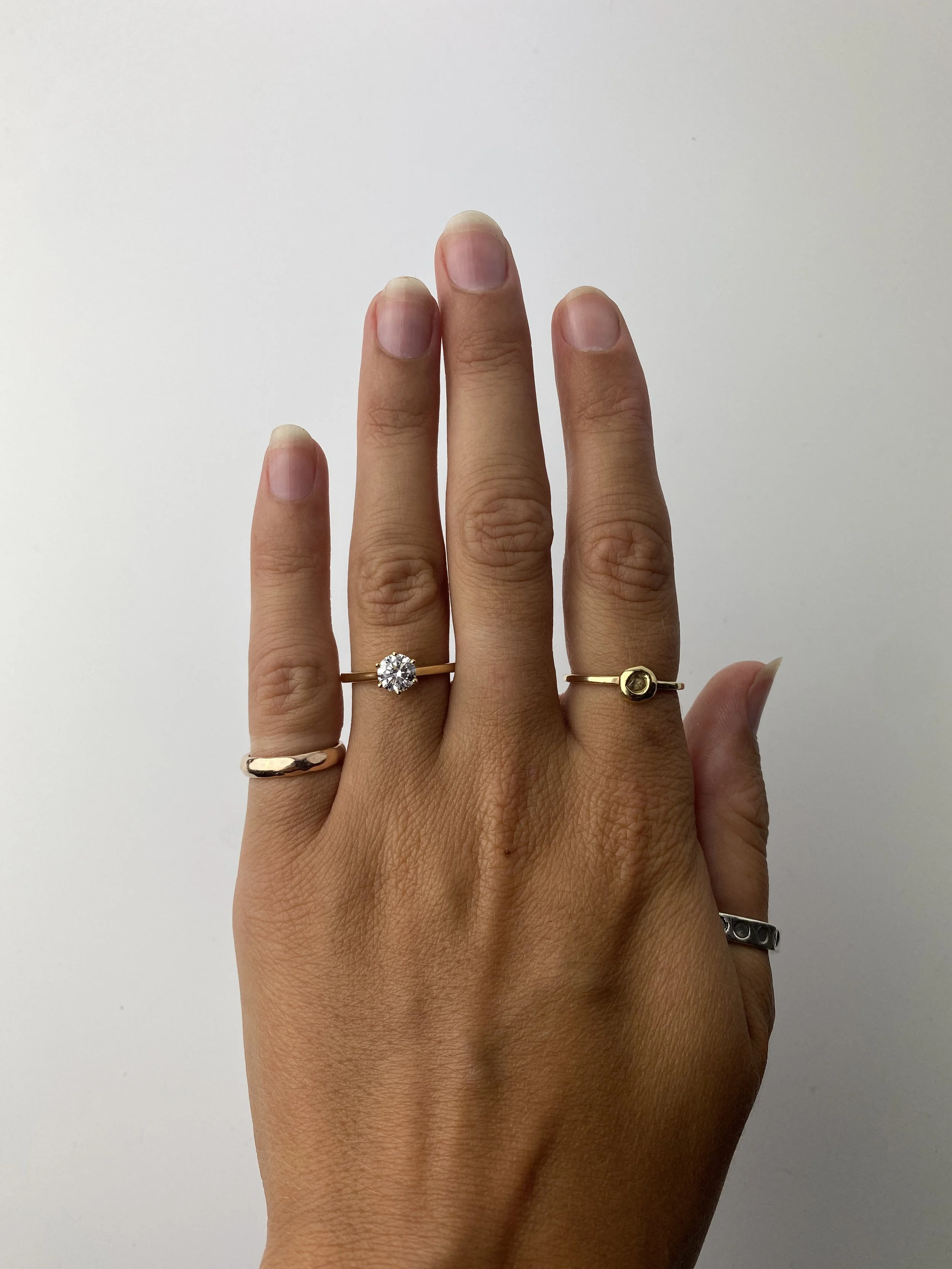 A person's left hand with four rings on different fingers, against a white background.