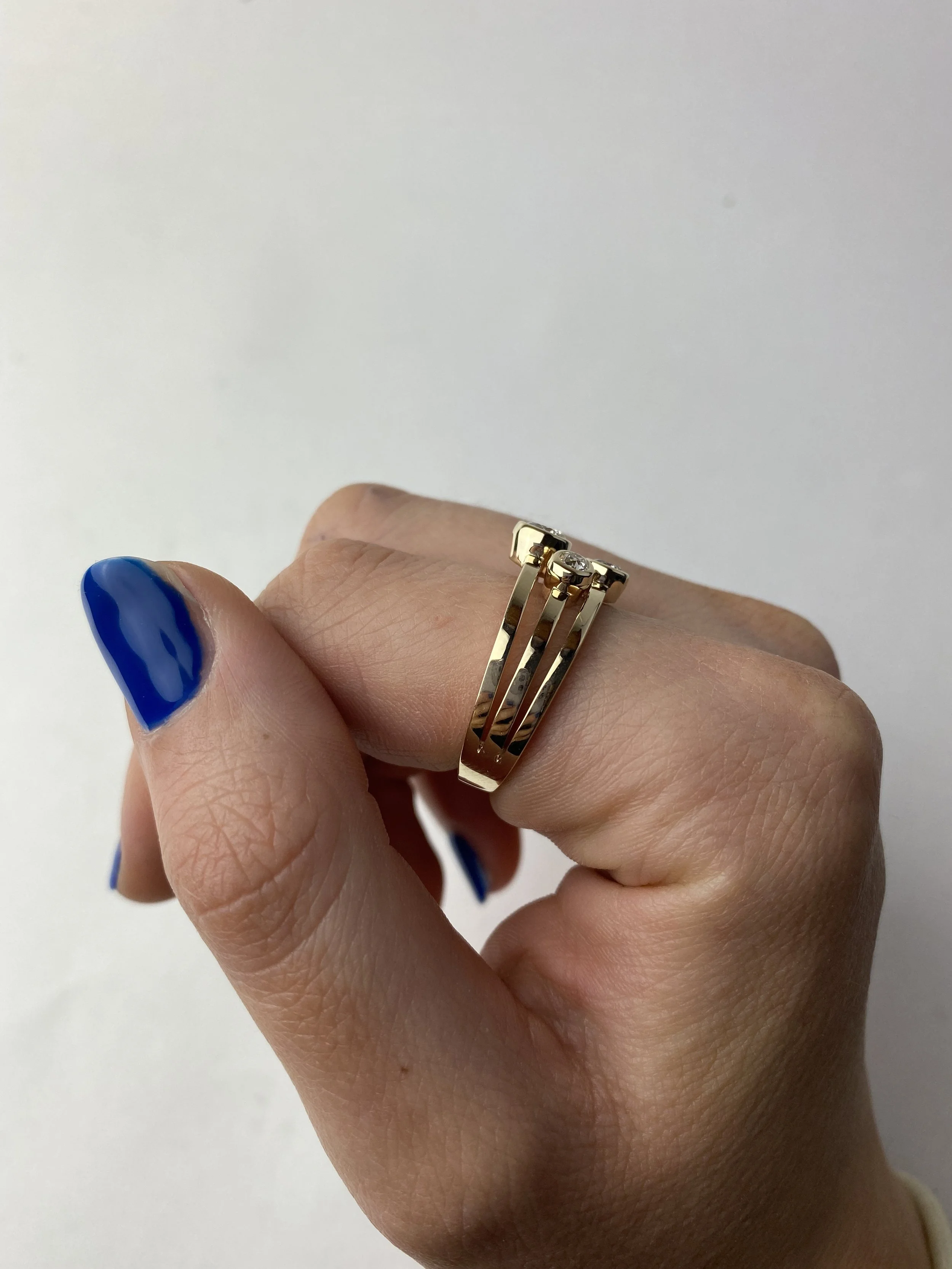 A hand with polished blue nails wearing two gold rings on the middle finger against a plain white background.