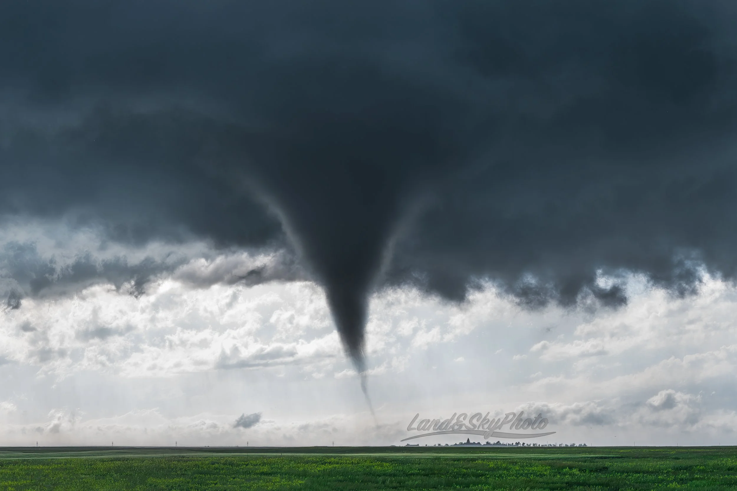 A backlit funnel dances in some Wyoming fields intermittently touching down next to a farmstead.
